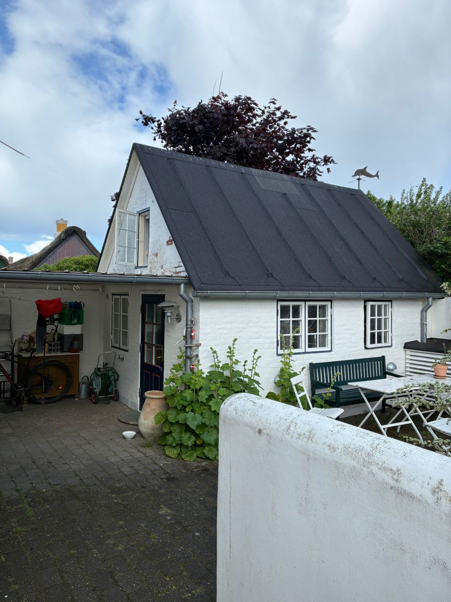 A small whitewashed annex with a black roof and a courtyard with a bench and table in Sønderho