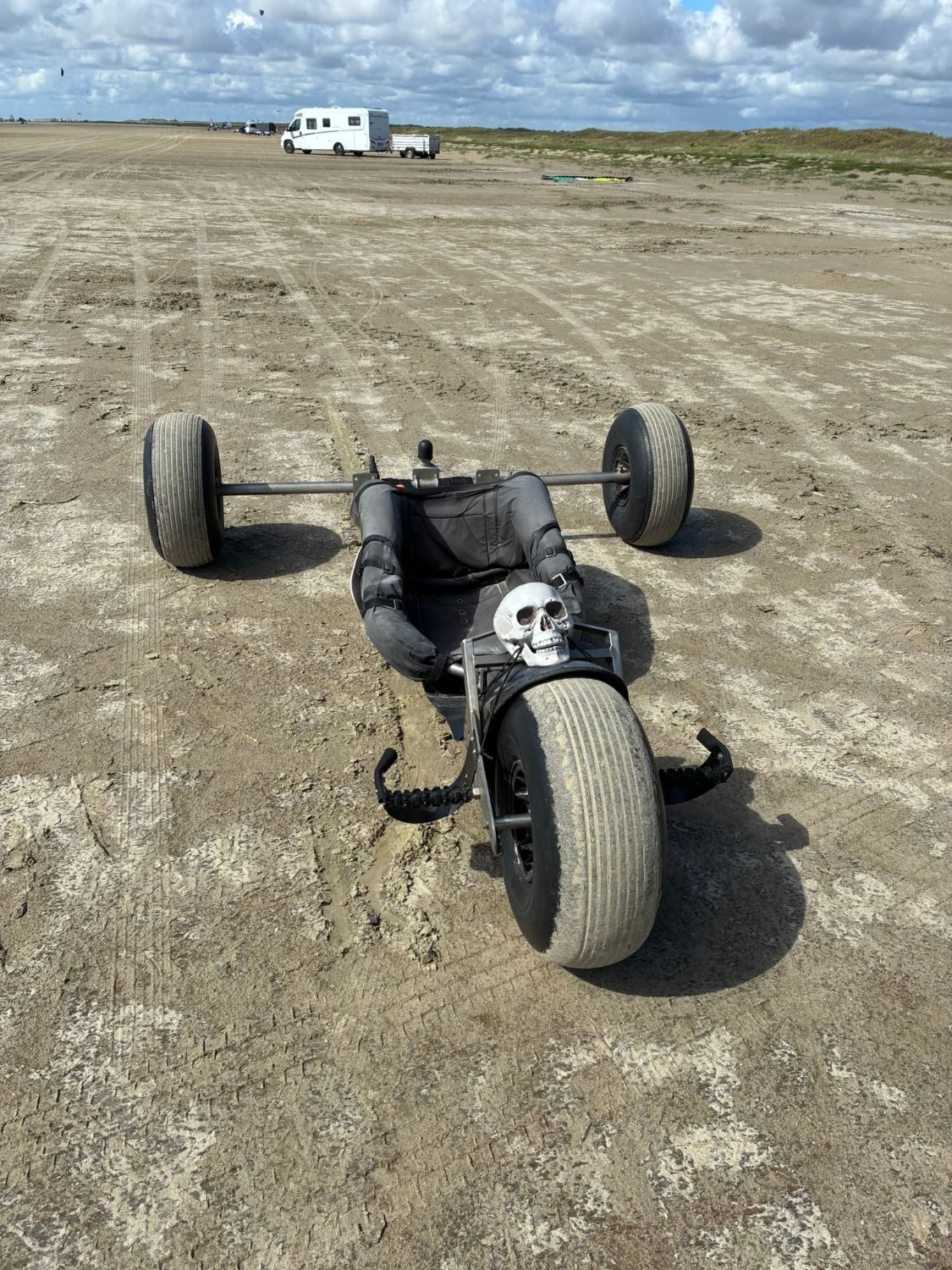 A kite buggy with fat tyres and a plastic skull on the front, parked on the hard sand of the beach