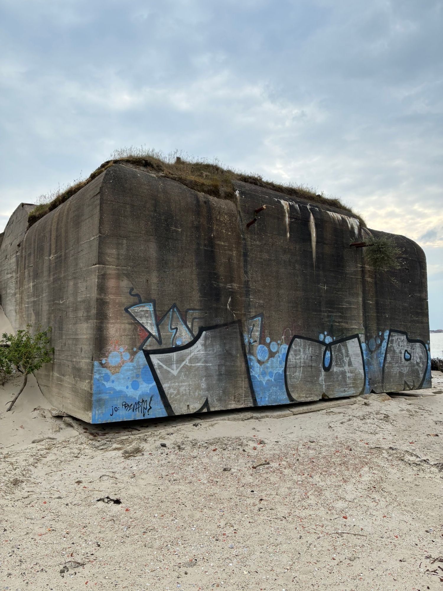 A massive old concrete bunker with blue and grey graffiti on the sand