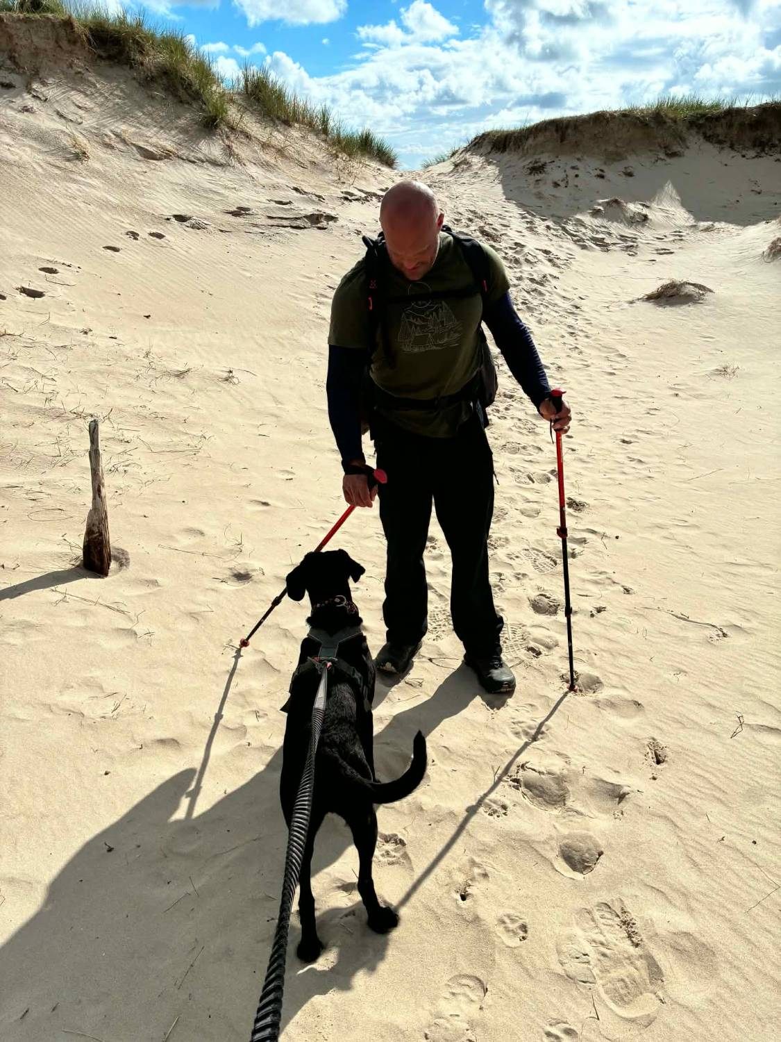 Leif with trekking poles greeting Maggie on a sandy path between grassy dunes