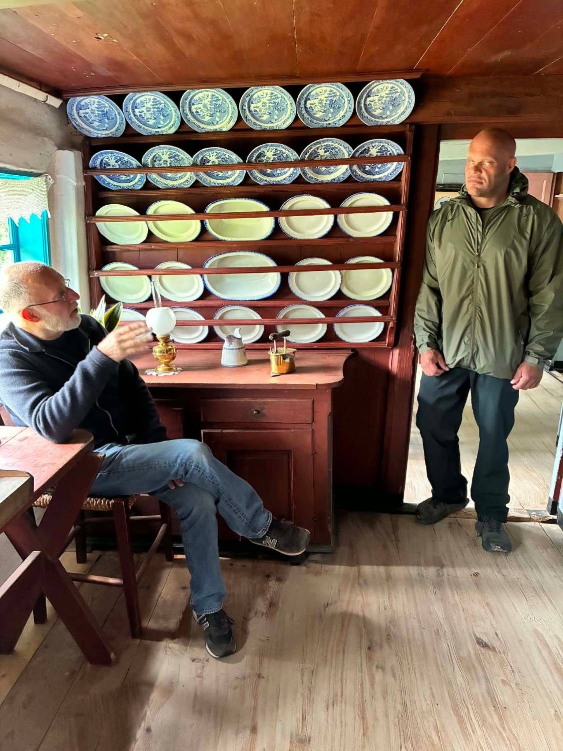 Our host sitting by a plate rack full of blue and white plates inside Hannes Hus, Leif standing in the doorway