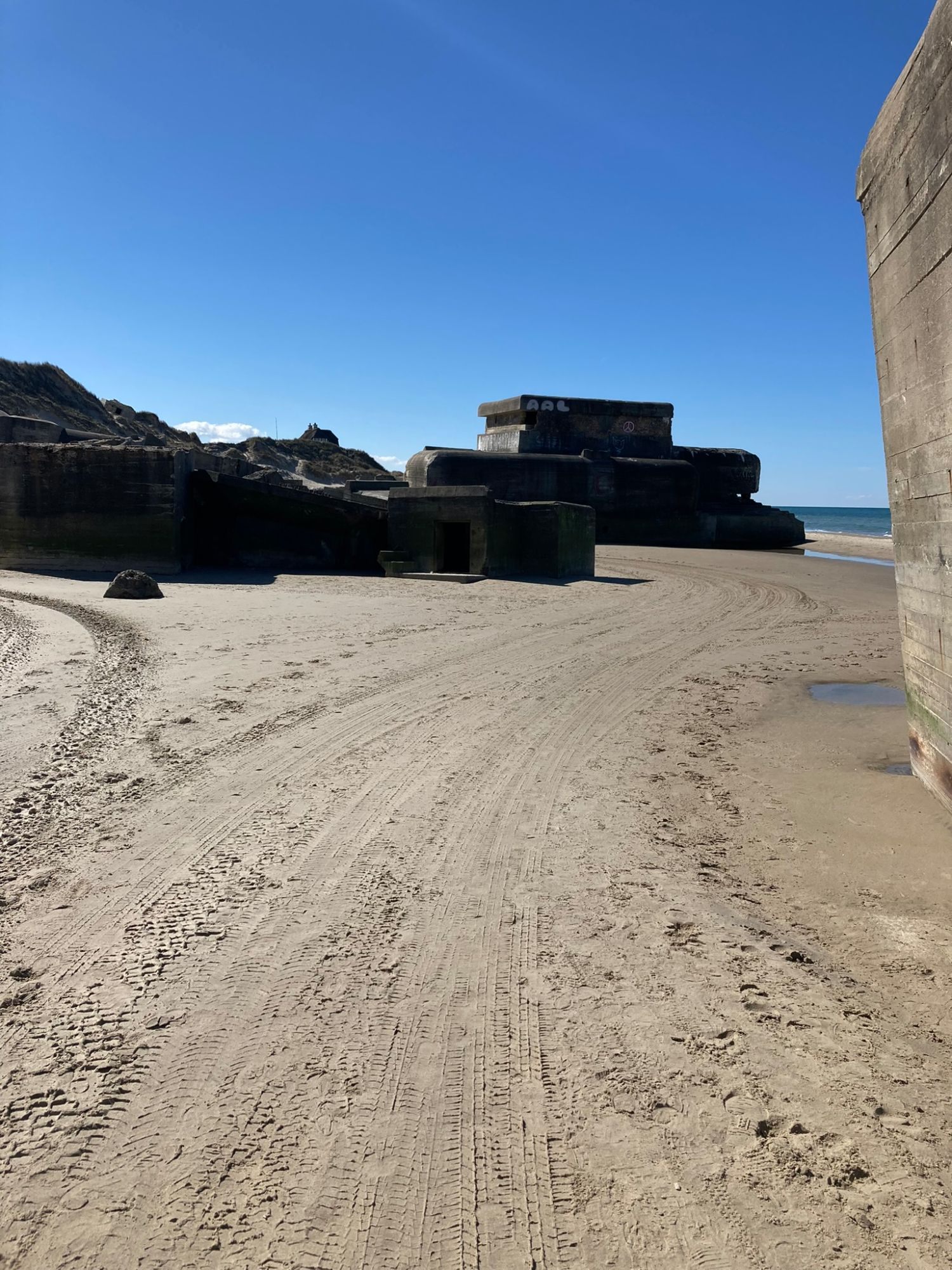 Old concrete bunkers on the sand below the dunes, with tyre tracks across the beach