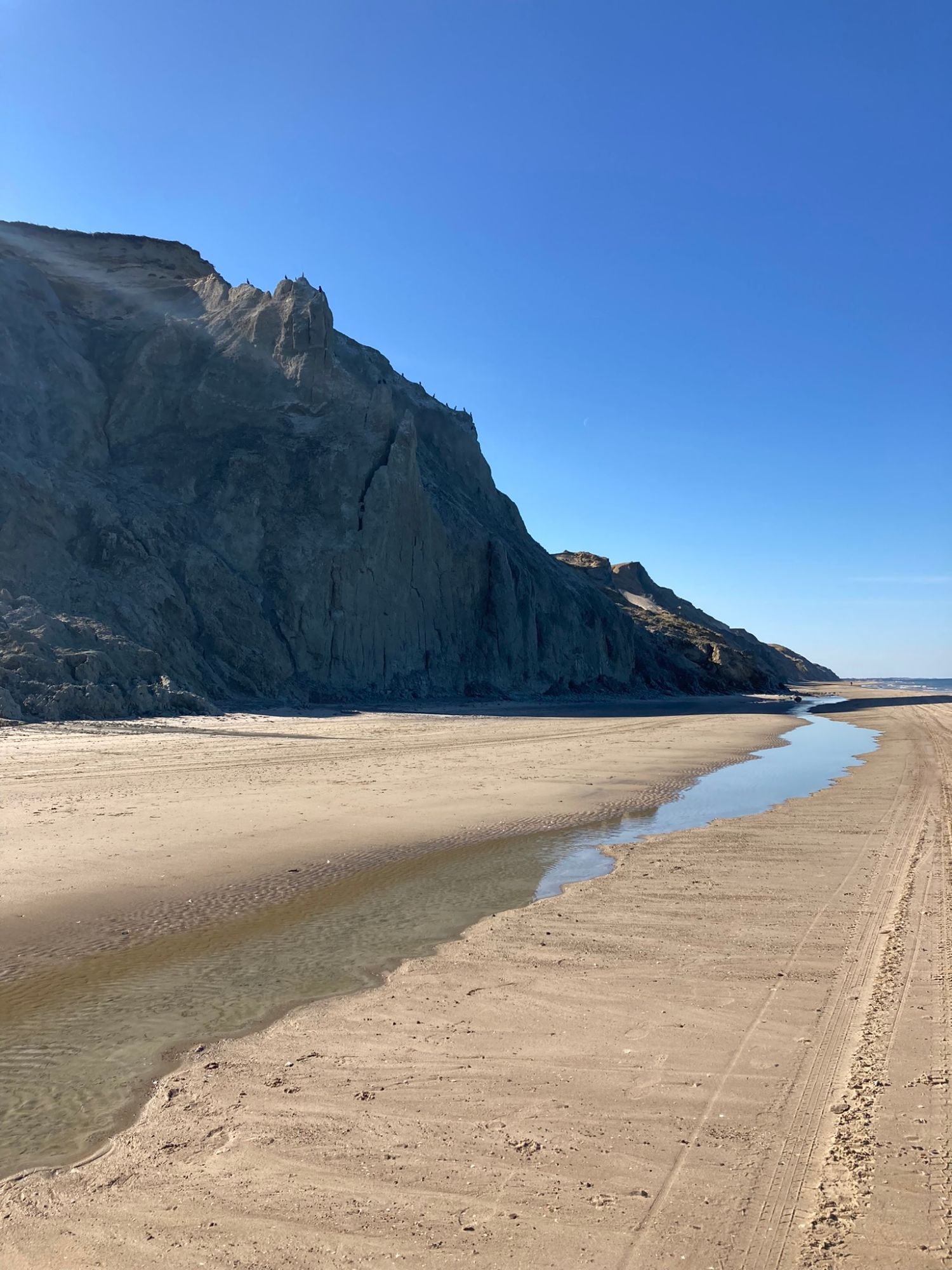 The high cliffs at Rubjerg Knude above a wide sandy beach with a shallow stream, under a clear blue sky