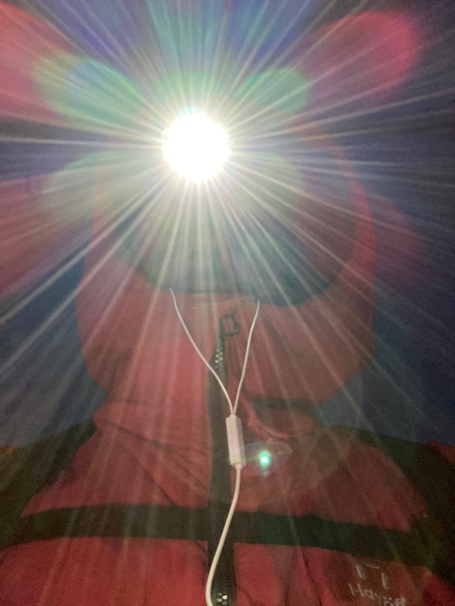 Selfie at night lit by a bright headlamp, wearing a red jacket and earphones