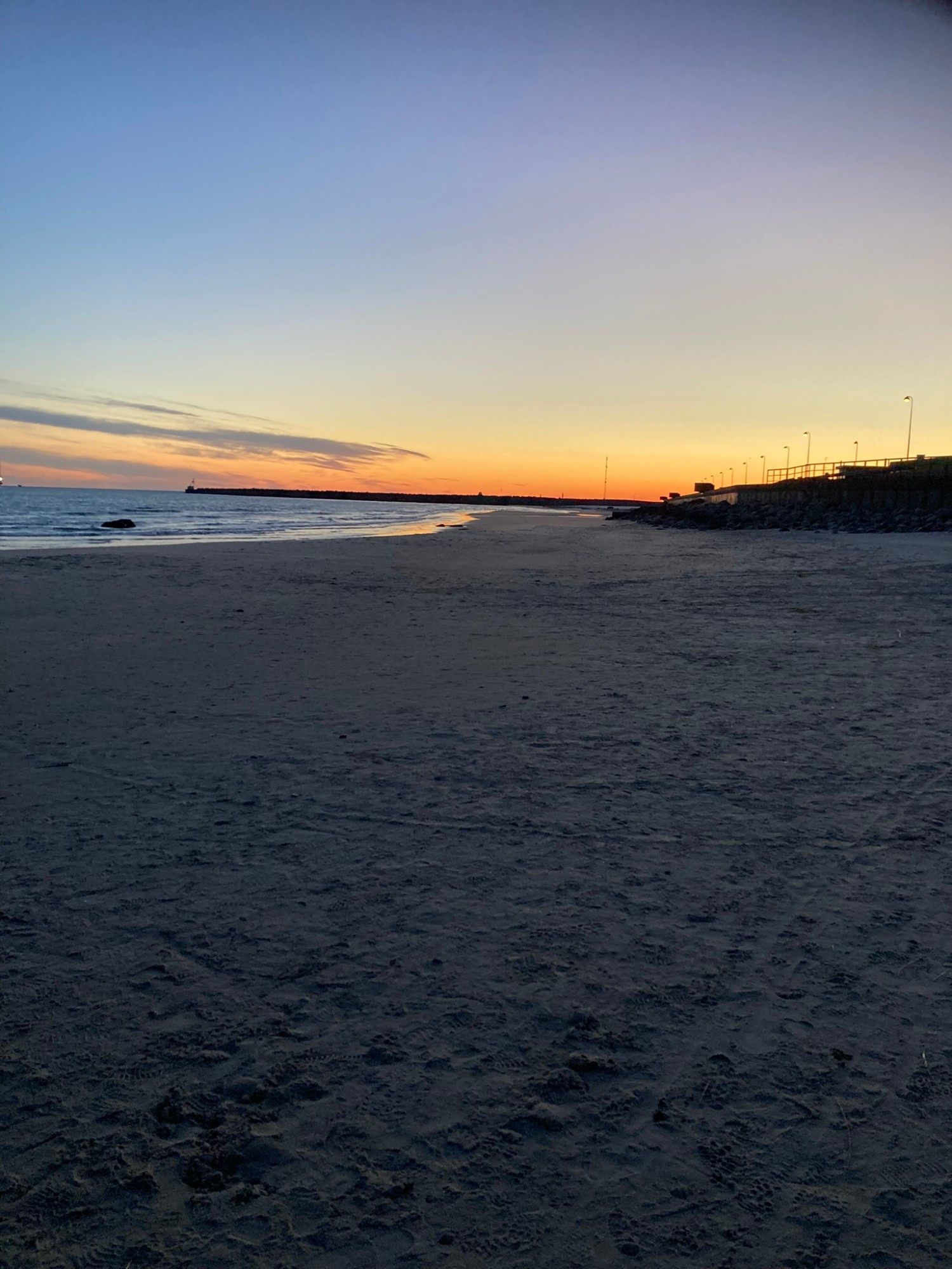 Empty beach at sunrise near Hirtshals harbour, with the pier and street lights on the right