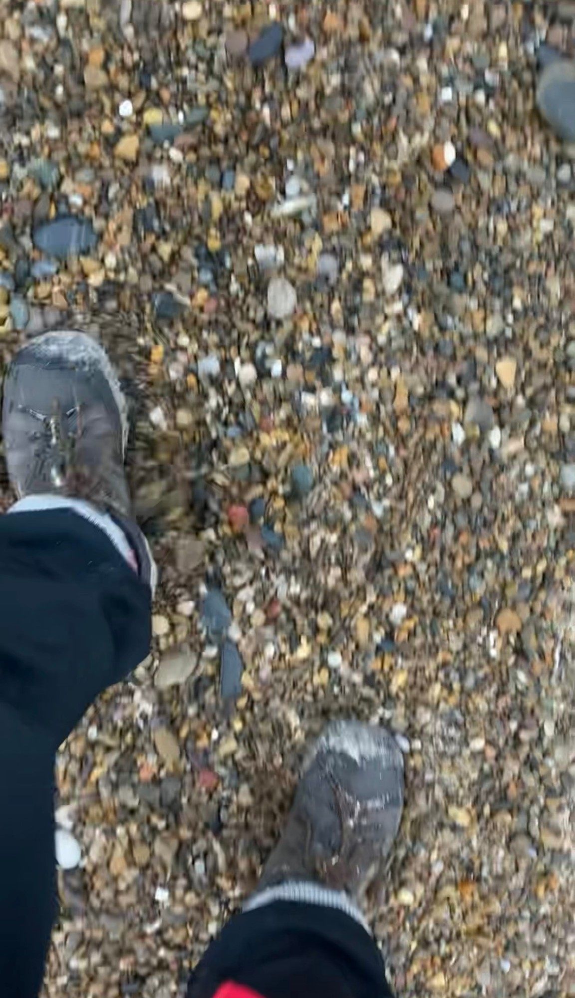 Looking down at my boots on a beach of loose, colourful pebbles