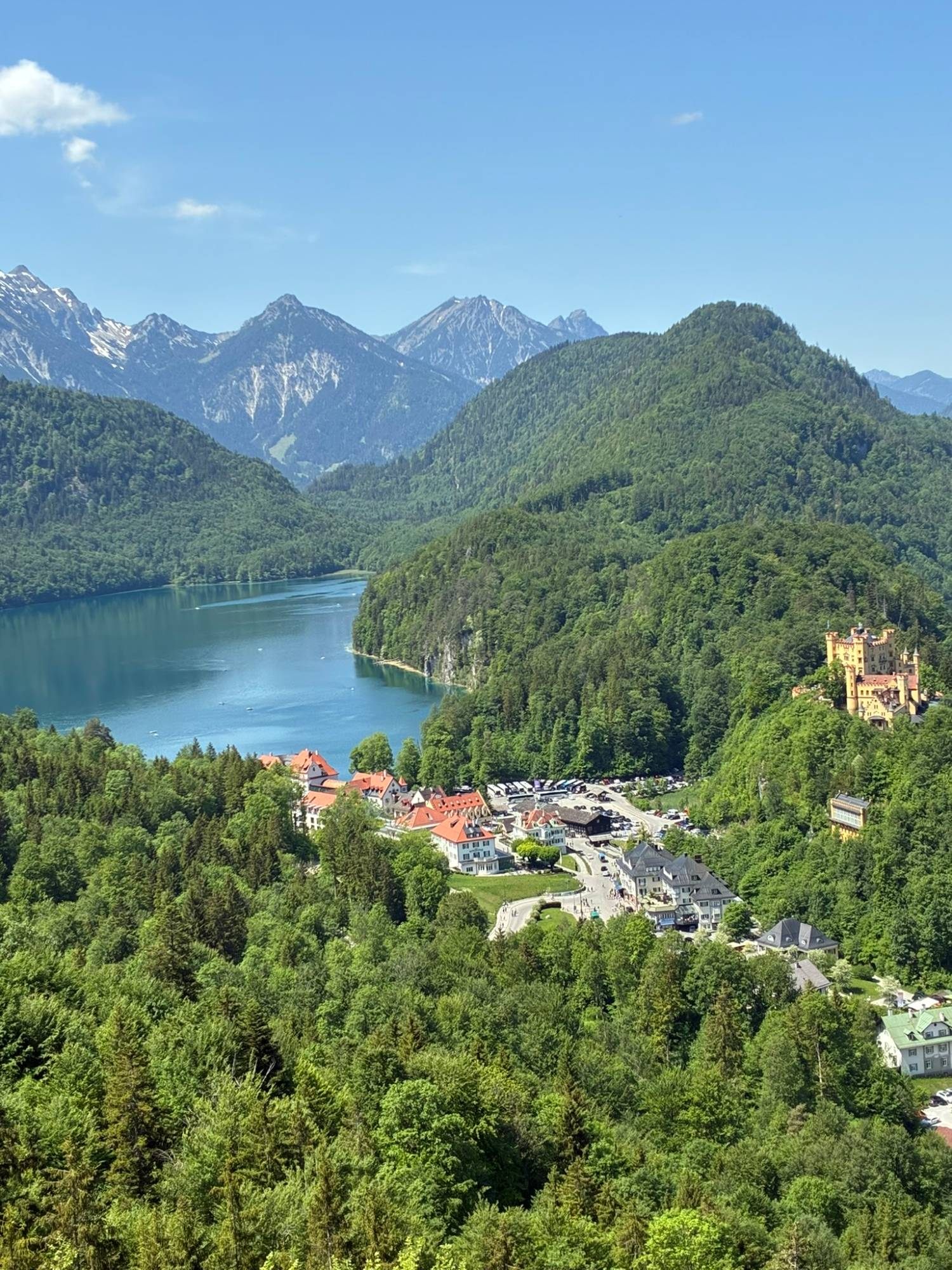 View from above of the blue Alpsee, the village and the yellow Hohenschwangau Castle among forested mountains