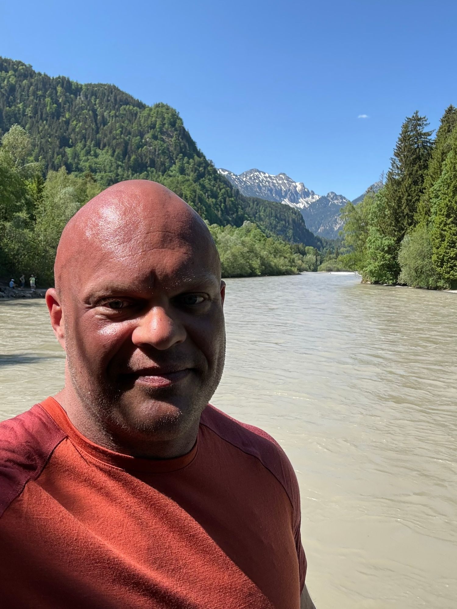 Selfie by the wide, milky-green river Lech with forested slopes and snowy peaks behind