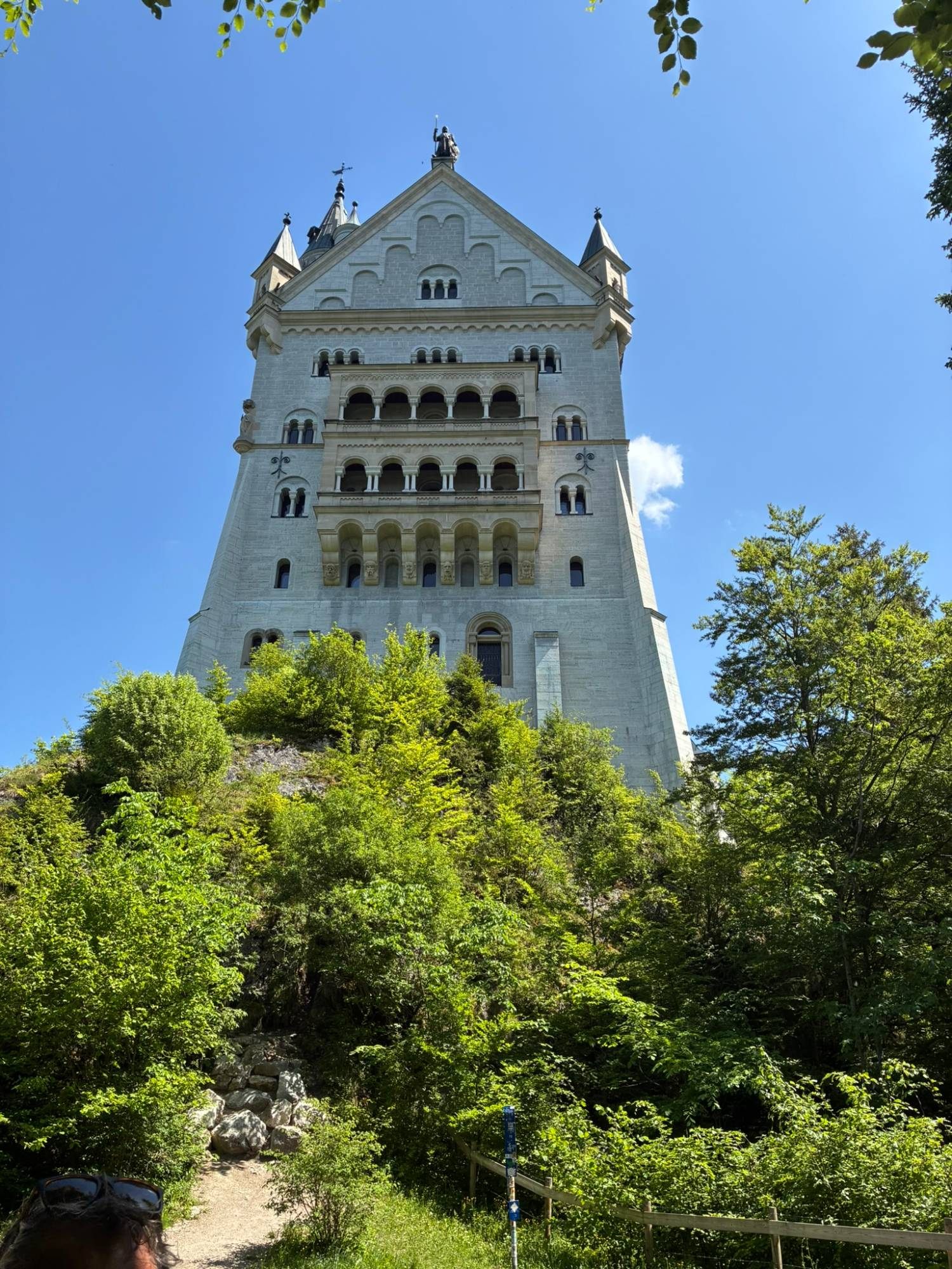 The tall white gable of Neuschwanstein Castle rising above trees on its rock