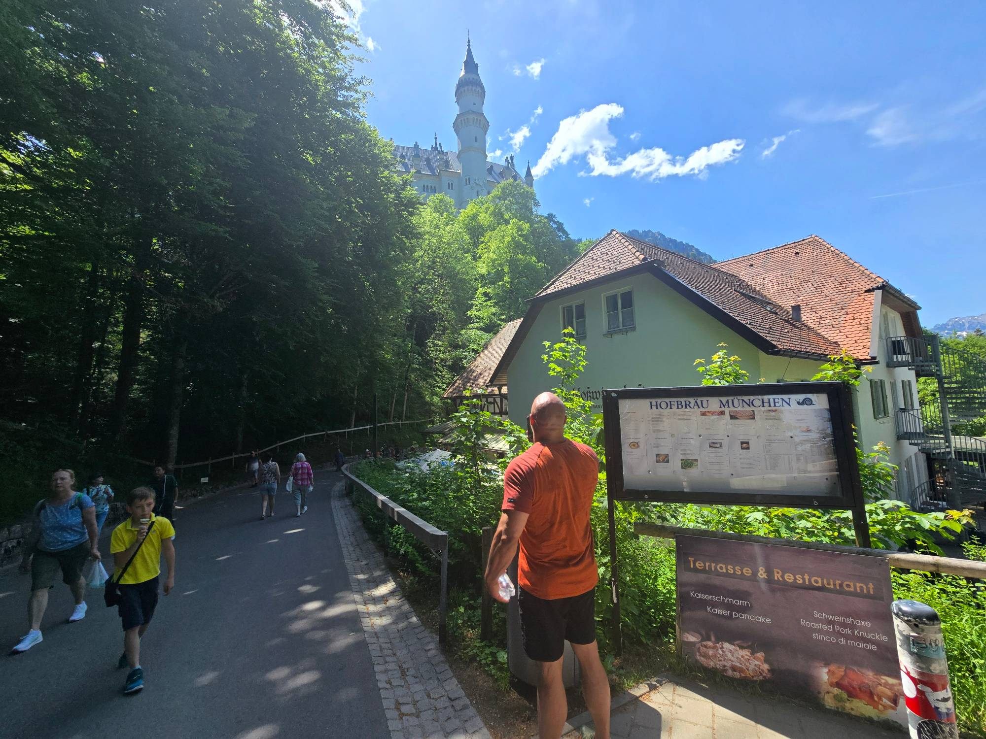 Walking up the road to Neuschwanstein past a restaurant, with the castle tower above the trees