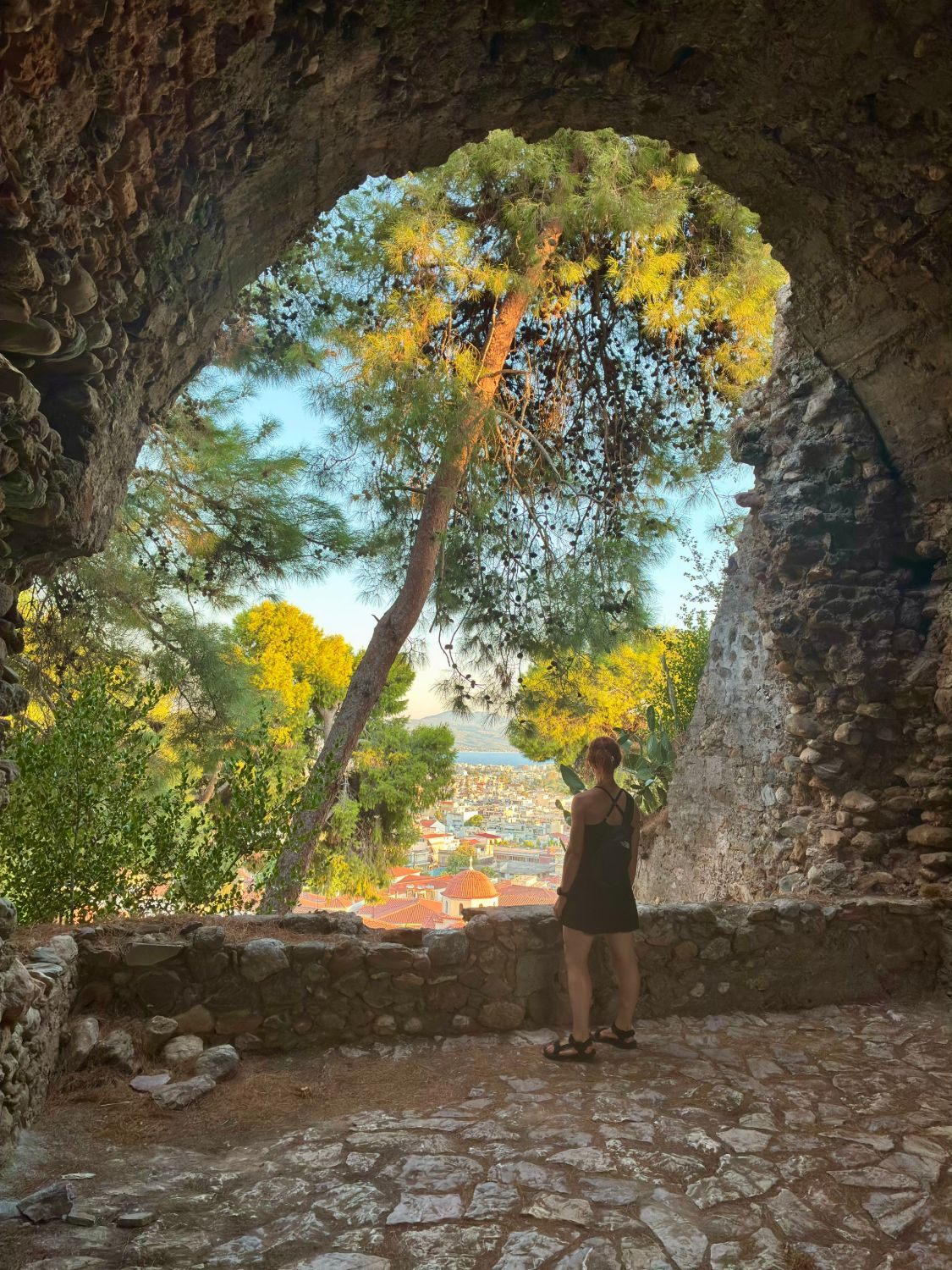 Kristine beneath a stone arch at Kalamata Castle looking out over the city