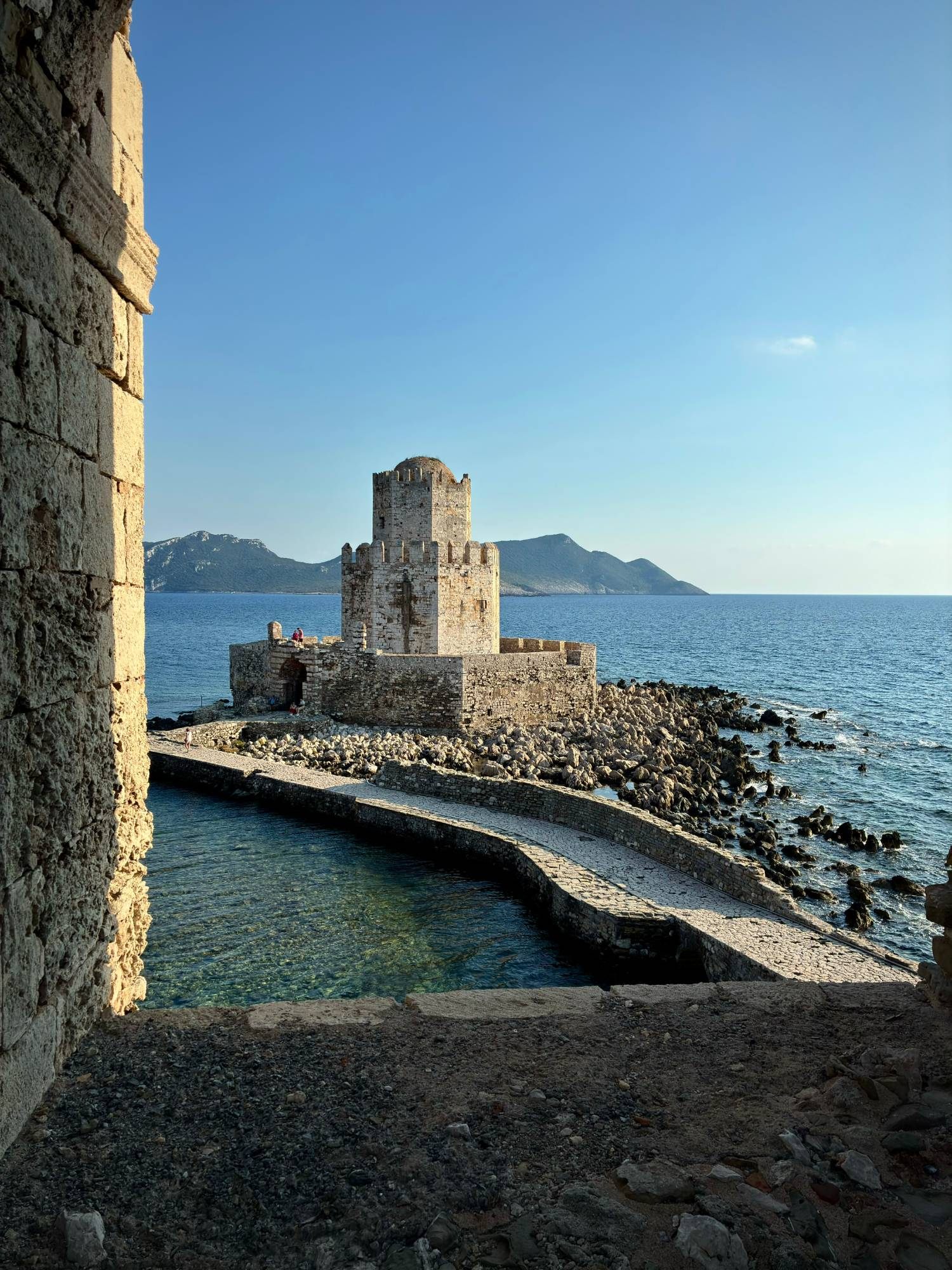The Bourtzi tower framed by the walls of Methoni Castle, with clear turquoise water below