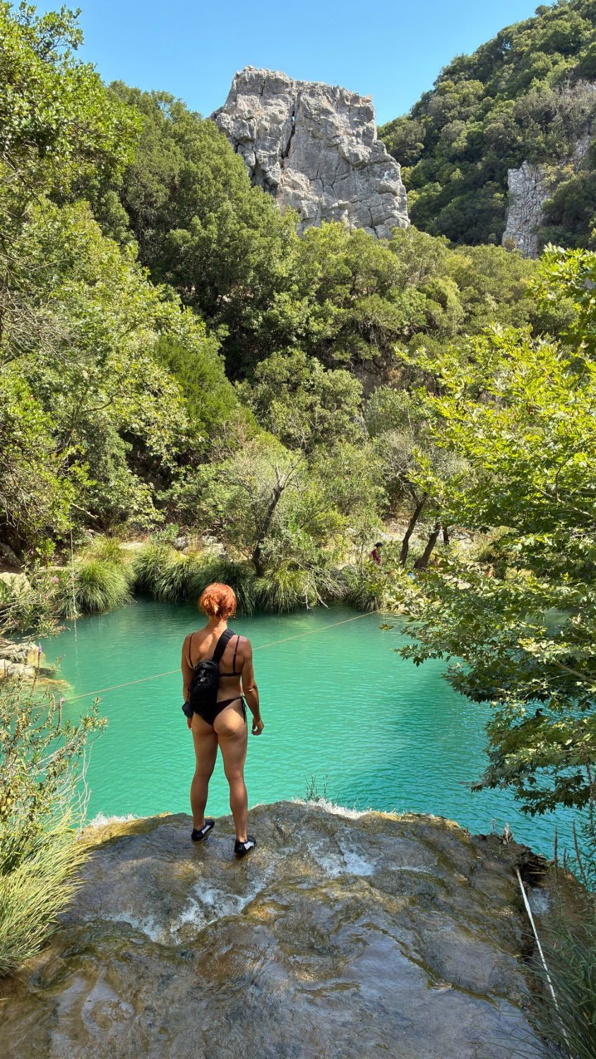 Kristine standing on top of Kadi Waterfall looking out over the turquoise pool, with the zipline across it