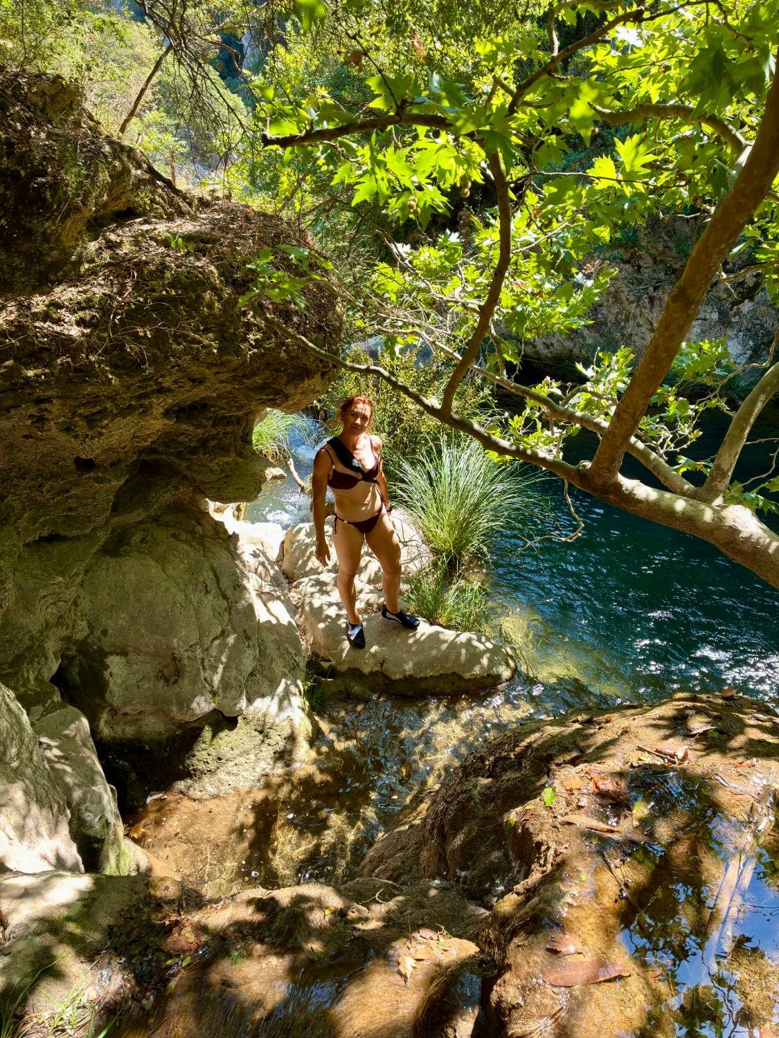 Kristine standing on rocks beside a clear stream and pool in dappled sunlight