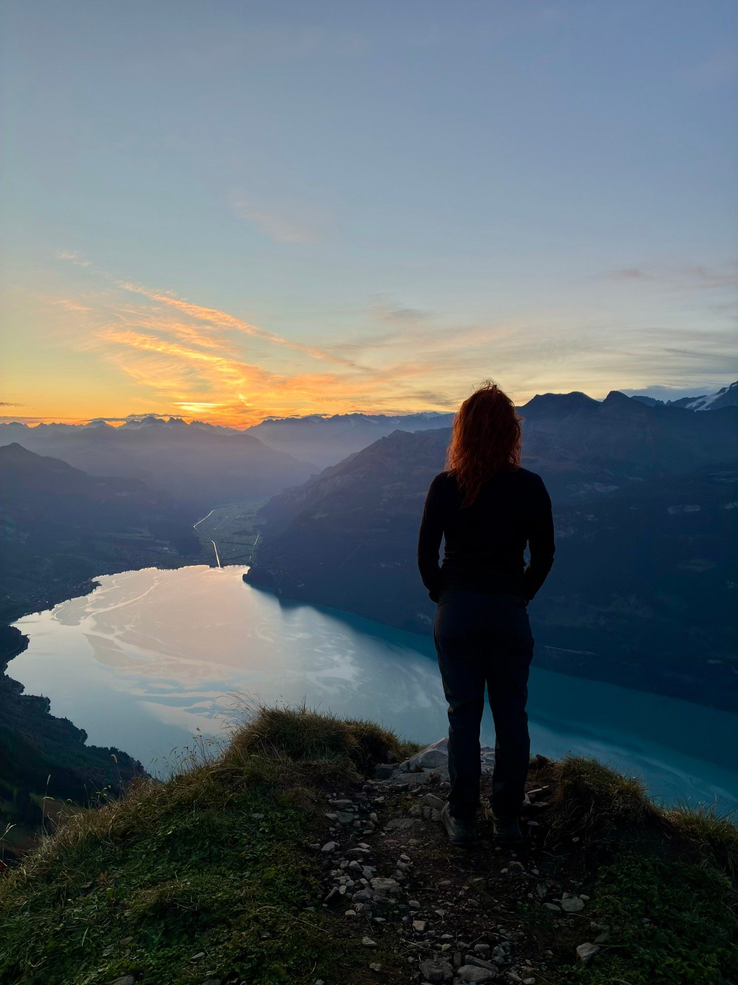 Kristine in silhouette on the ridge, looking out over Lake Brienz as the sky glows orange