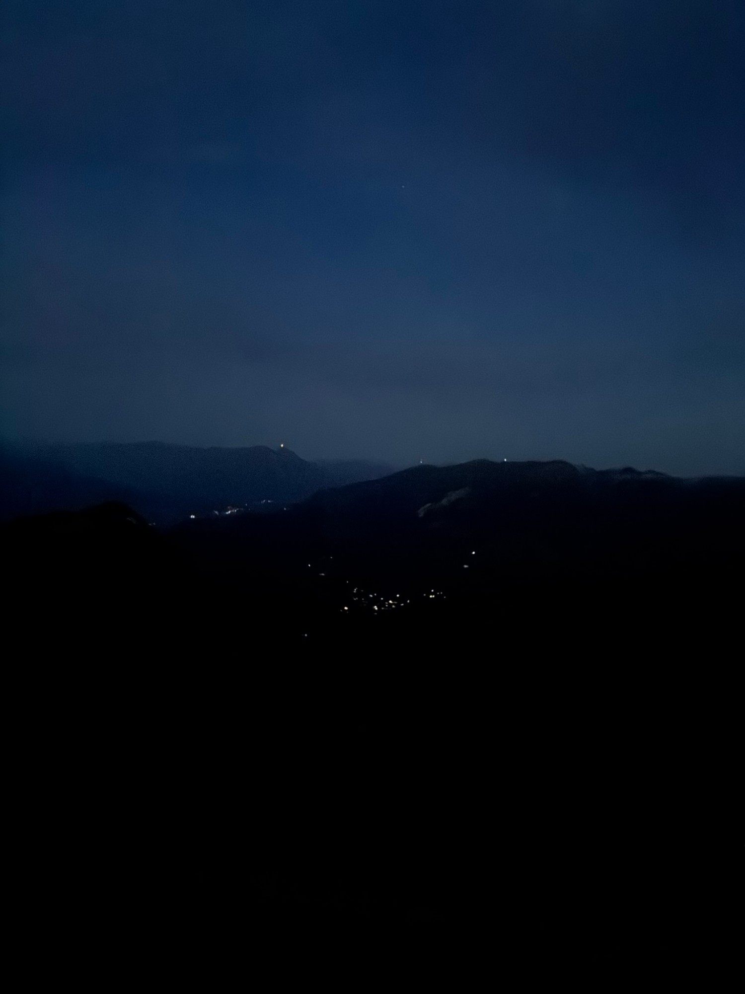 Dark mountain silhouettes and the lights of a village in the valley below before dawn