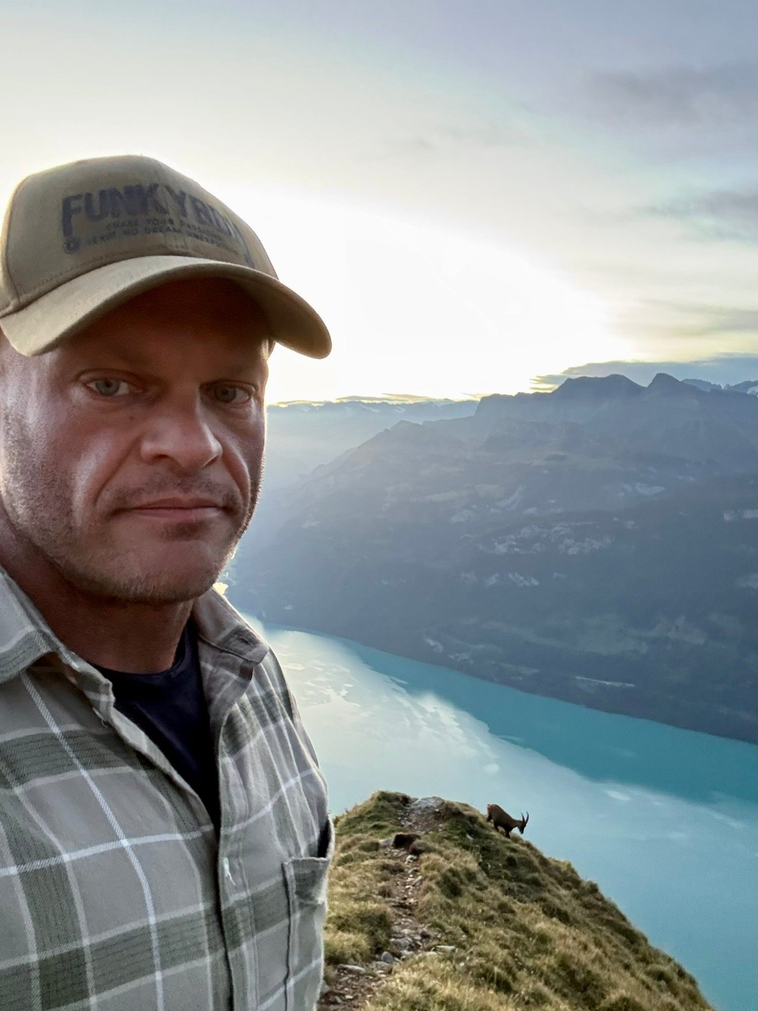 Selfie on the ridge with a wild ibex grazing on the edge behind, above Lake Brienz