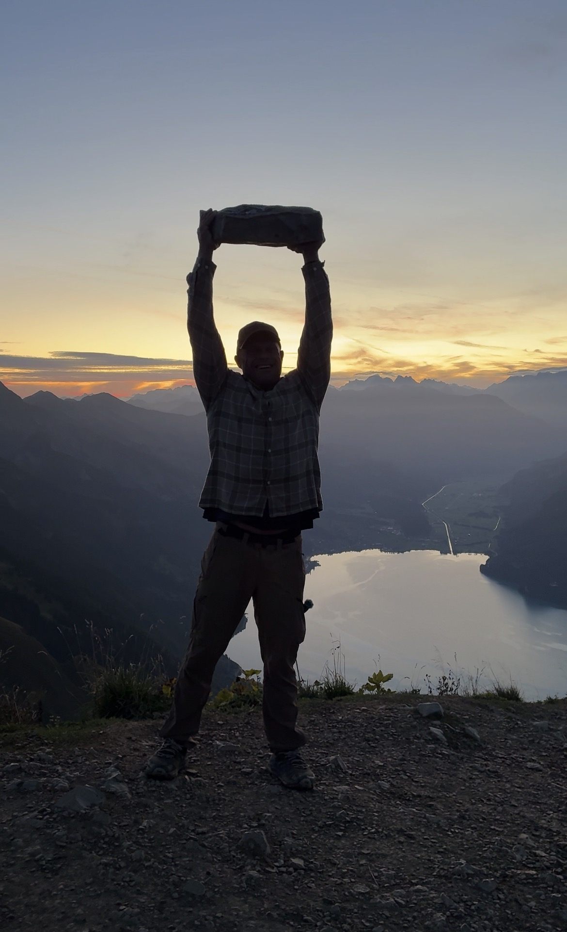 Silhouette lifting a stone overhead on the Augstmatthorn at dawn, with Lake Brienz and the Alps behind