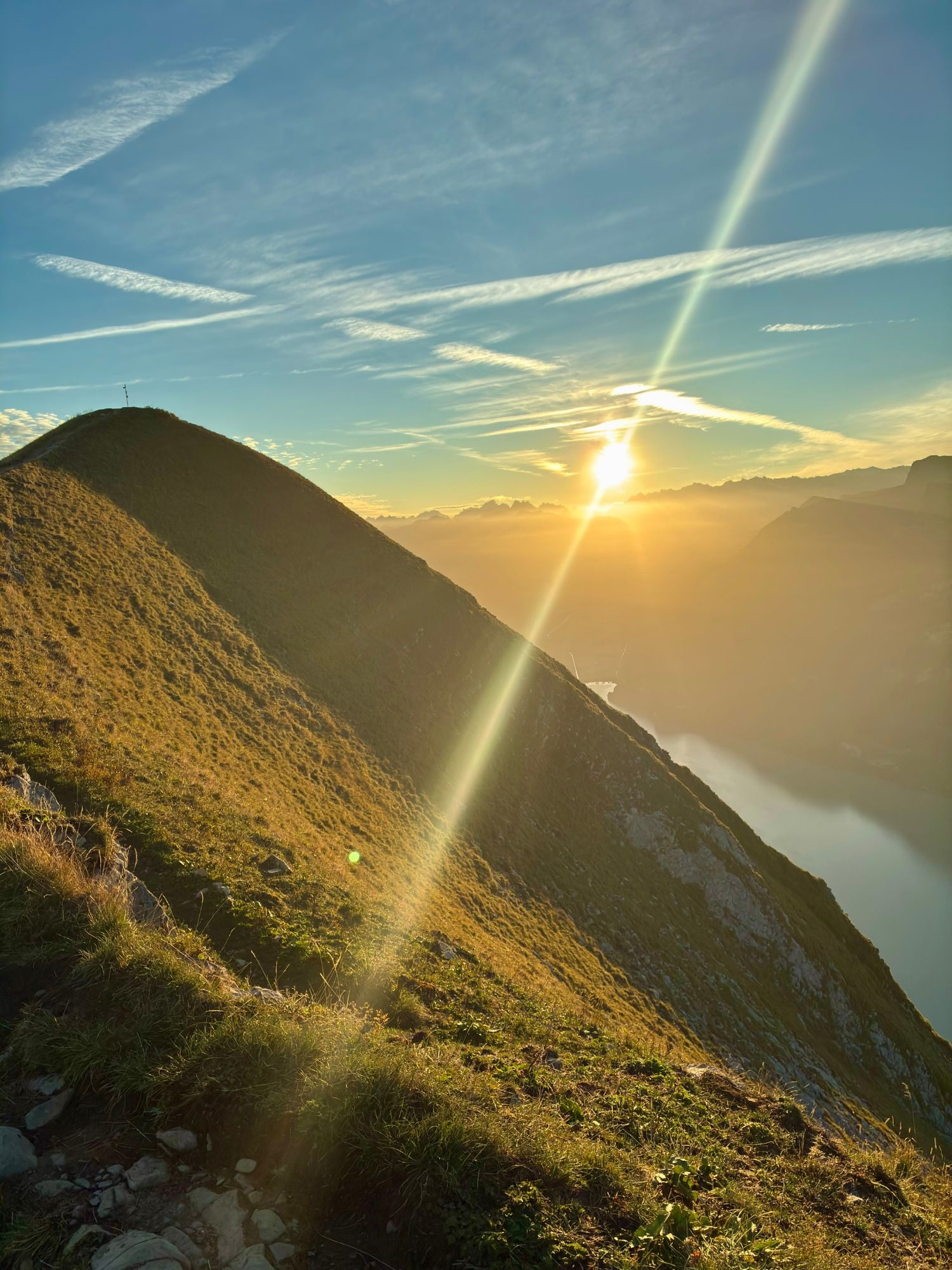 The sun rising behind the grassy summit ridge of the Augstmatthorn, with sun rays and the lake below
