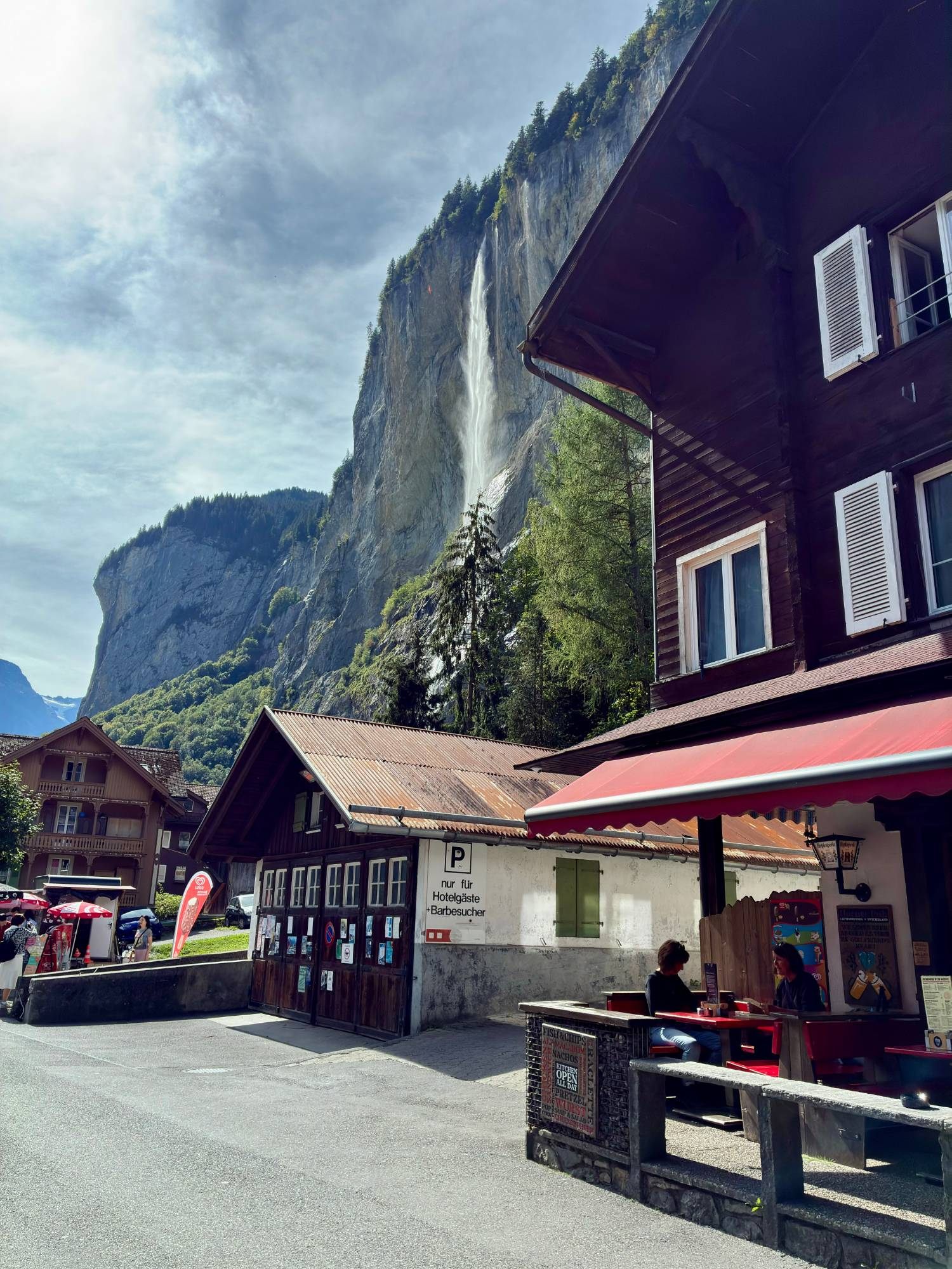 The Horner Pub in Lauterbrunnen with its red awning, and Staubbach Falls dropping down the cliff behind it