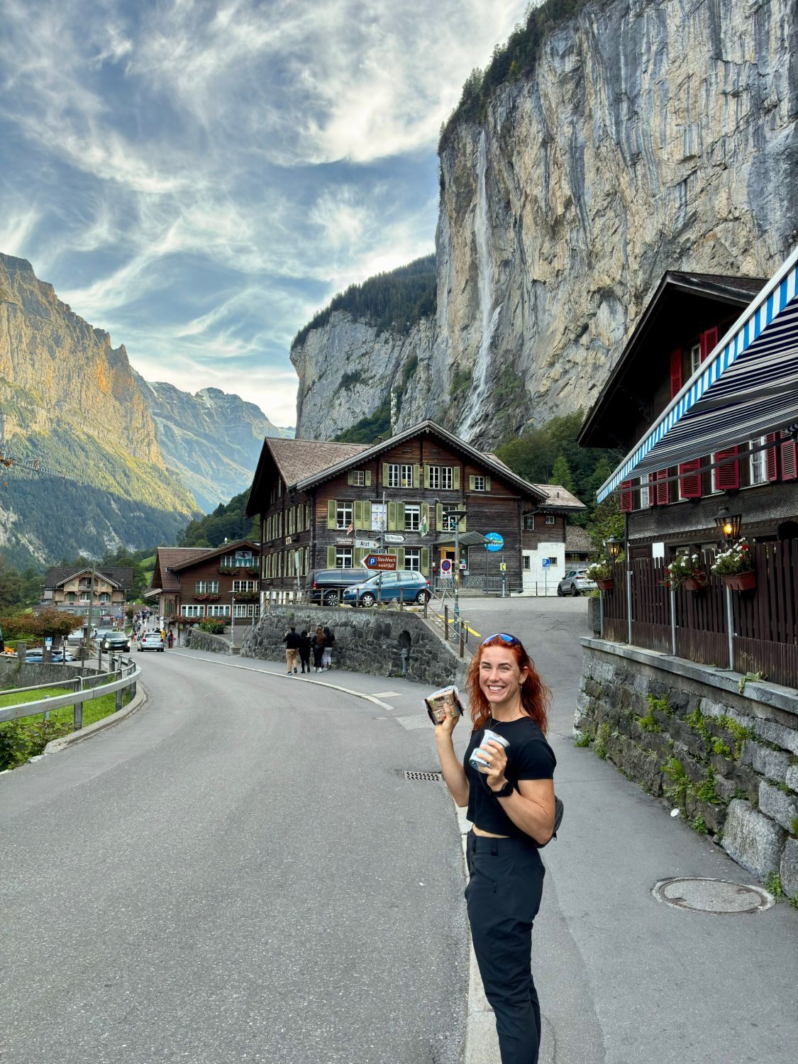 Kristine smiling on the main street of Lauterbrunnen with wooden chalets and Staubbach Falls on the cliff behind