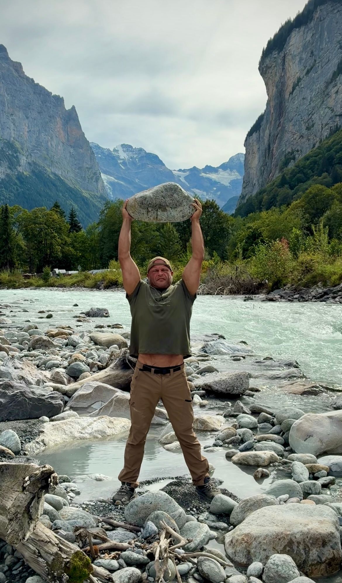 Lifting a large river stone overhead on the rocky bank of the Weisse Lütschine, with cliffs and mountains behind