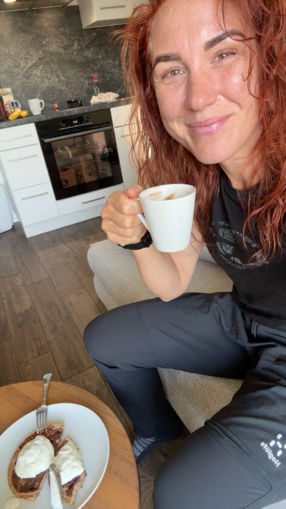 Kristine smiling with a cup of coffee and a plate of pancakes with yoghurt in the Airbnb kitchen