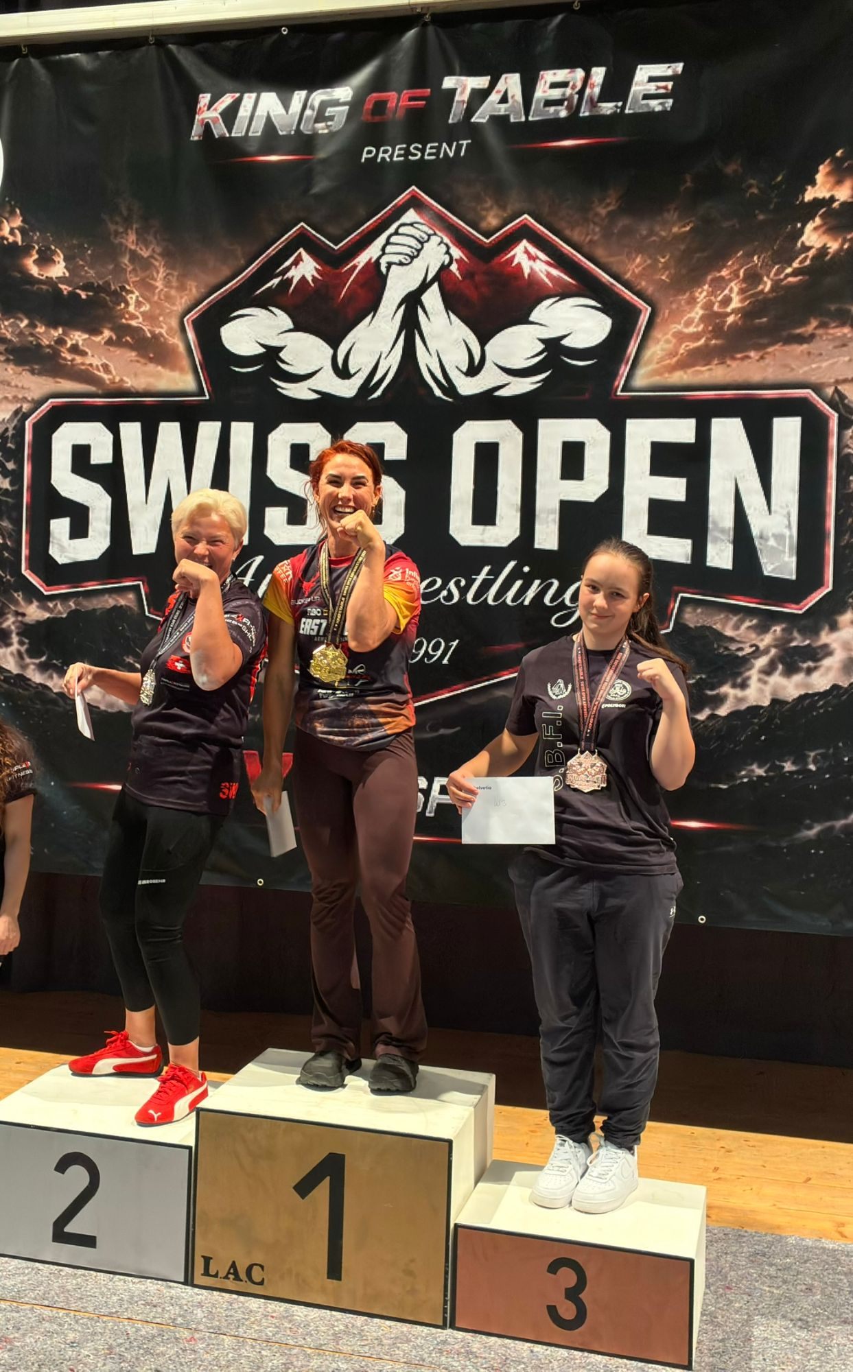 Kristine laughing on the top step of the Swiss Open podium with a gold medal, between the silver and bronze medallists