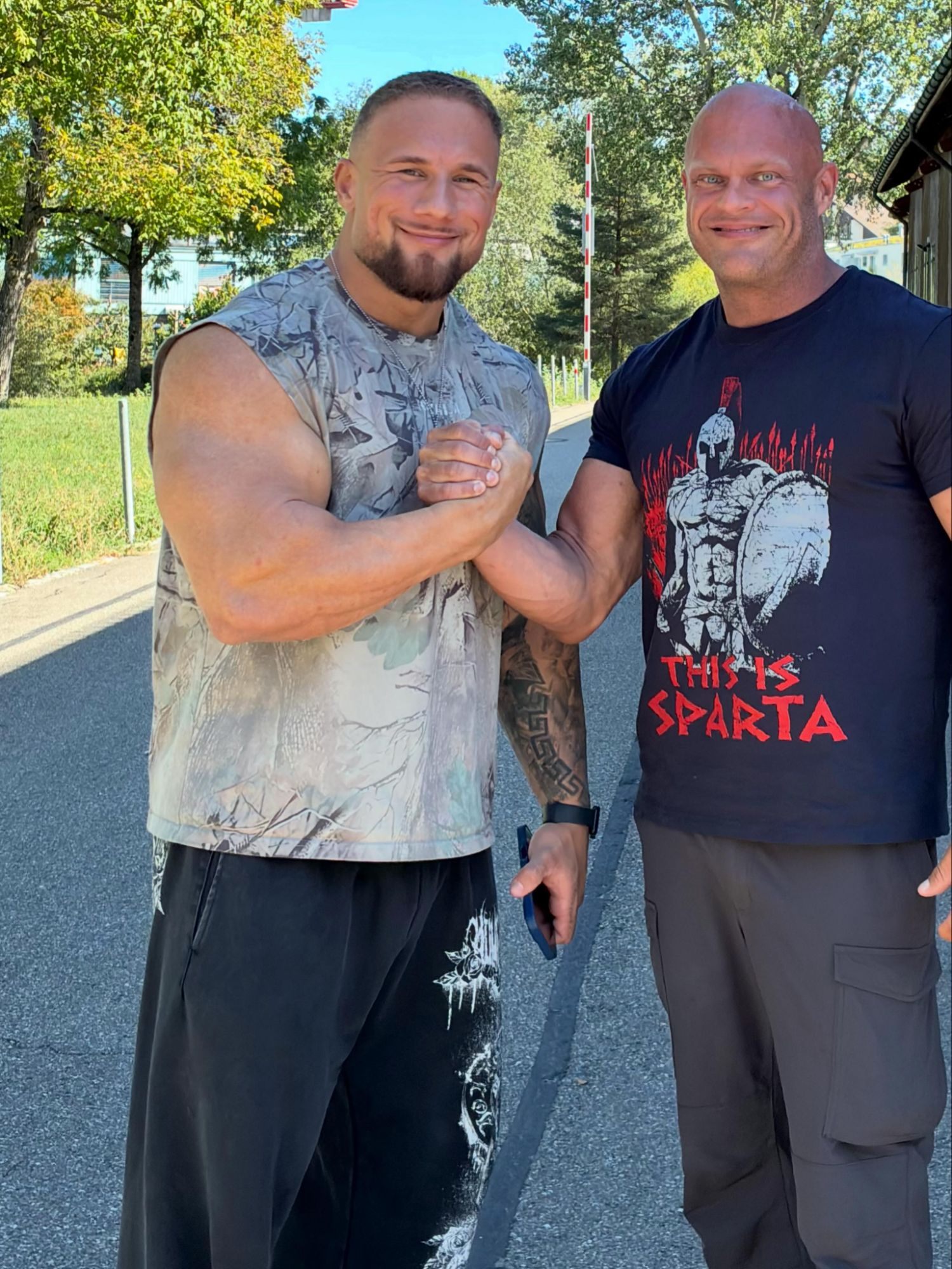 Leif and Leonidas Arkona in a sleeveless camo top clasping hands outside the hall