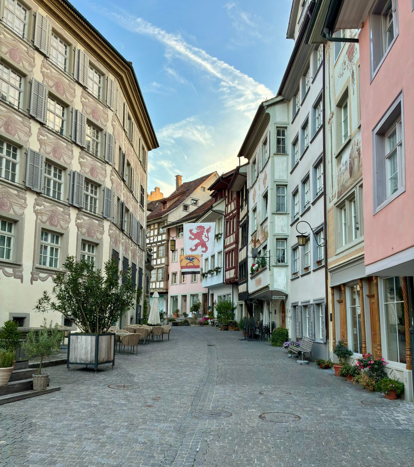 A cobbled street in Wil's old town with painted façades, flower pots and a red lion flag