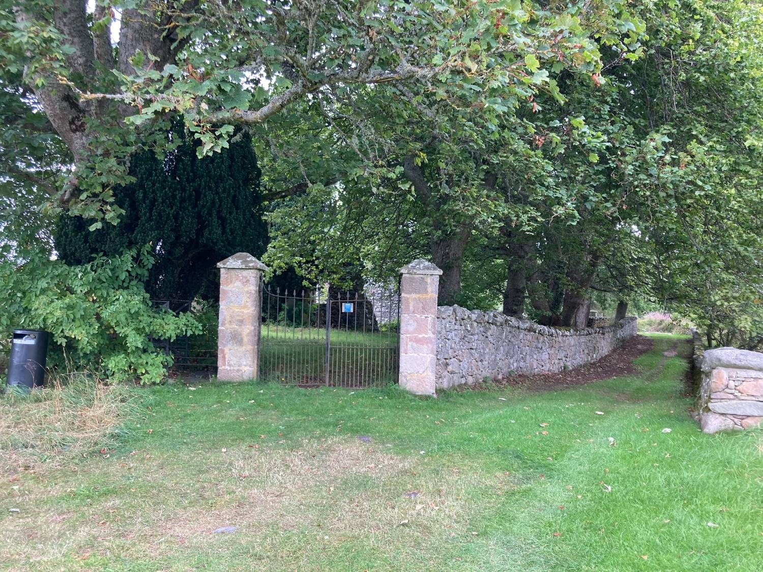 Stone gateposts and an iron gate in a dry-stone wall under large trees at the old Barevan churchyard