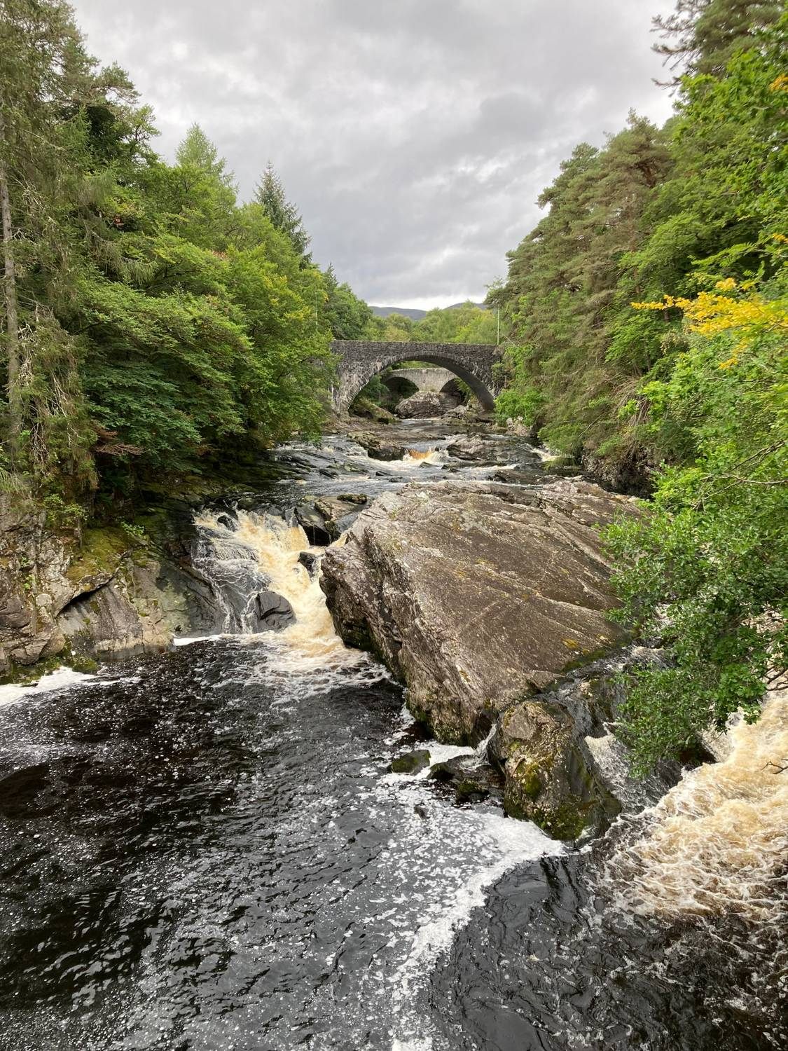 The River Moriston rushing over rocks below two stone bridges, framed by trees