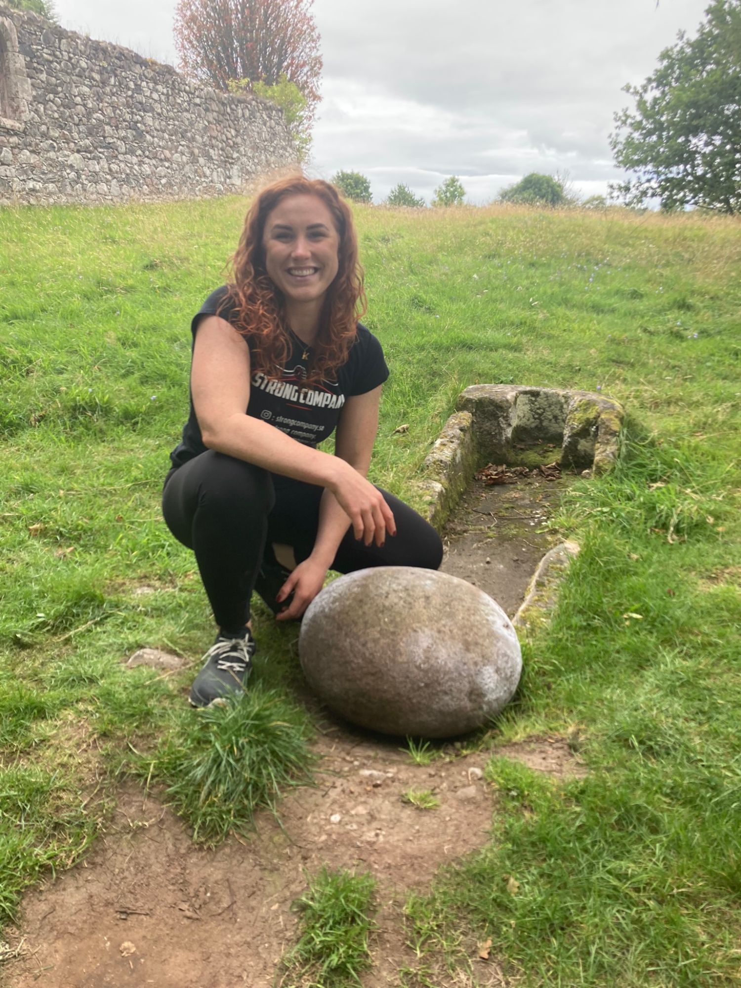 Kristine smiling, crouched beside the Barevan lifting stone and the stone sarcophagus