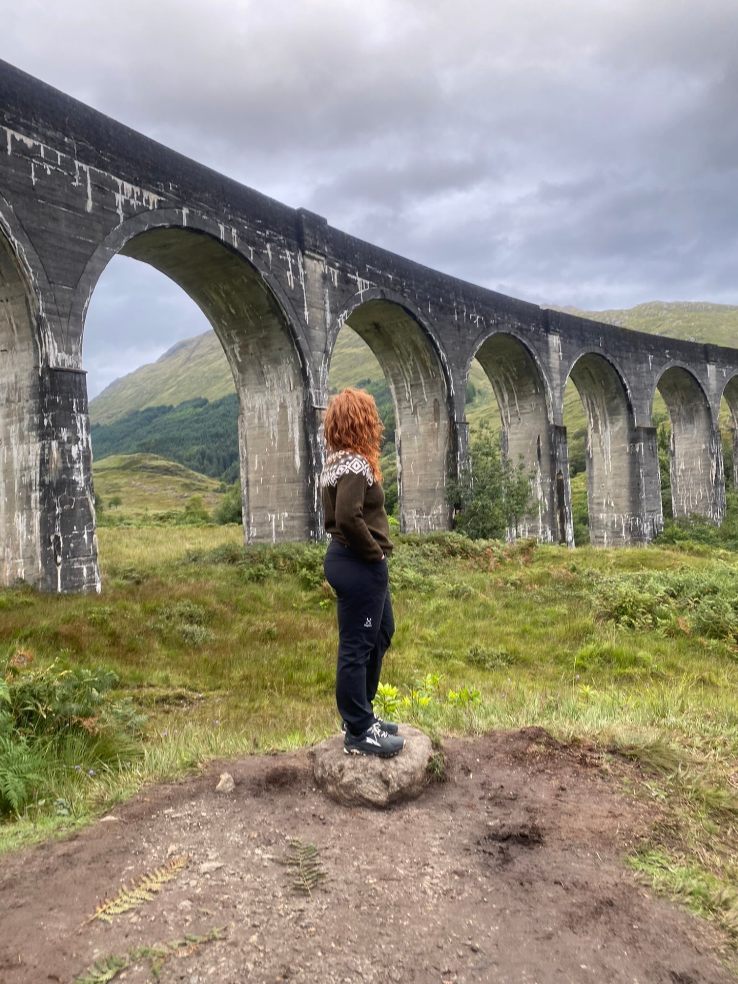 Kristine standing on a rock looking up at the tall arches of Glenfinnan Viaduct