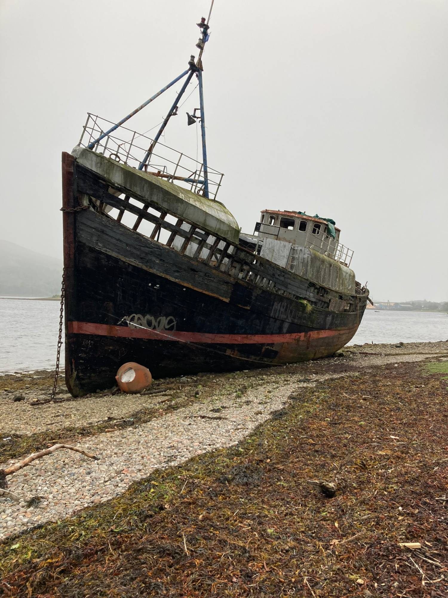 The black and red hull of the Old Boat of Caol seen from the bow, with Loch Linnhe behind in the mist