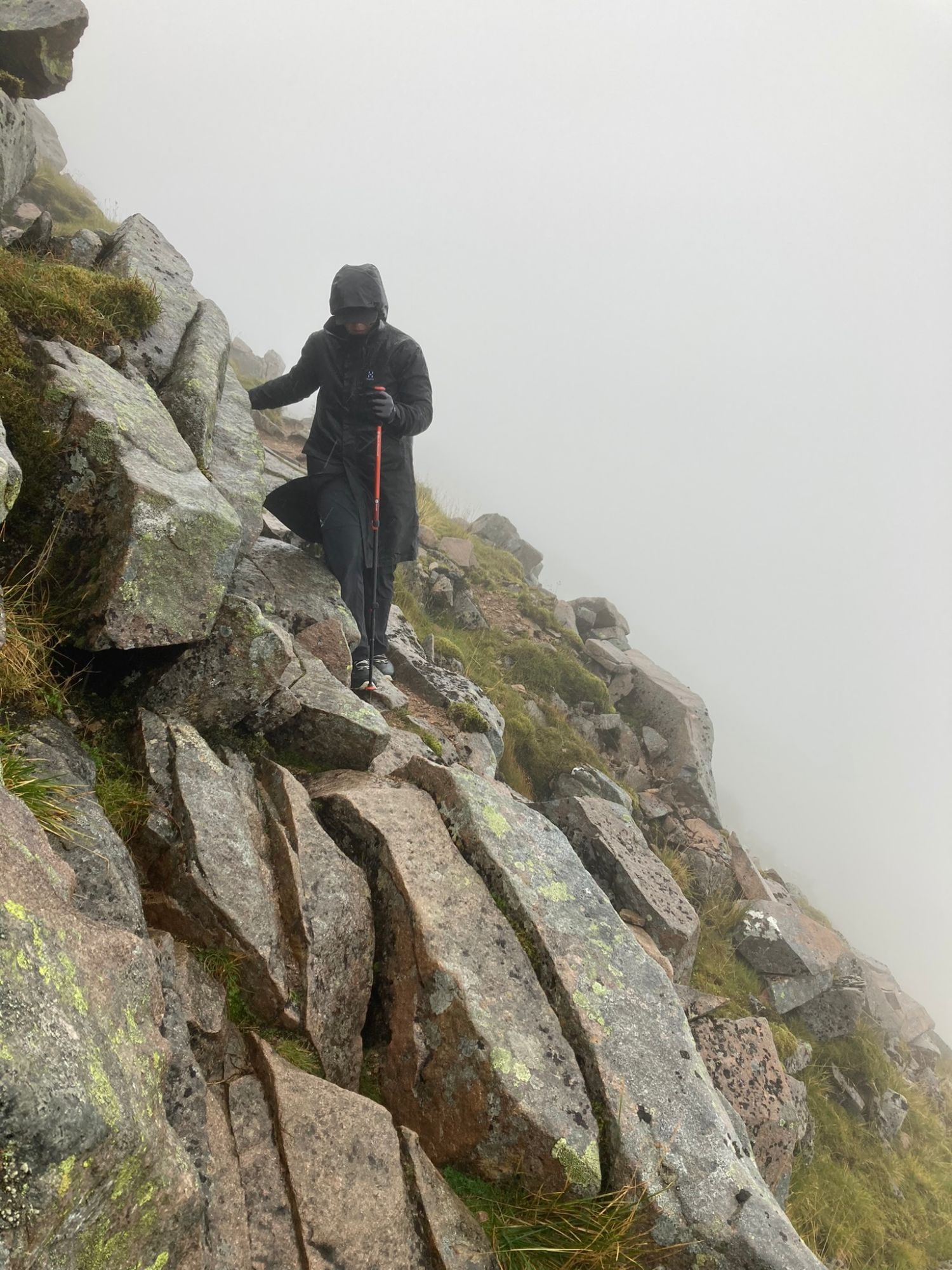 Kristine in a long rain jacket with a red trekking pole picking her way down granite slabs in fog
