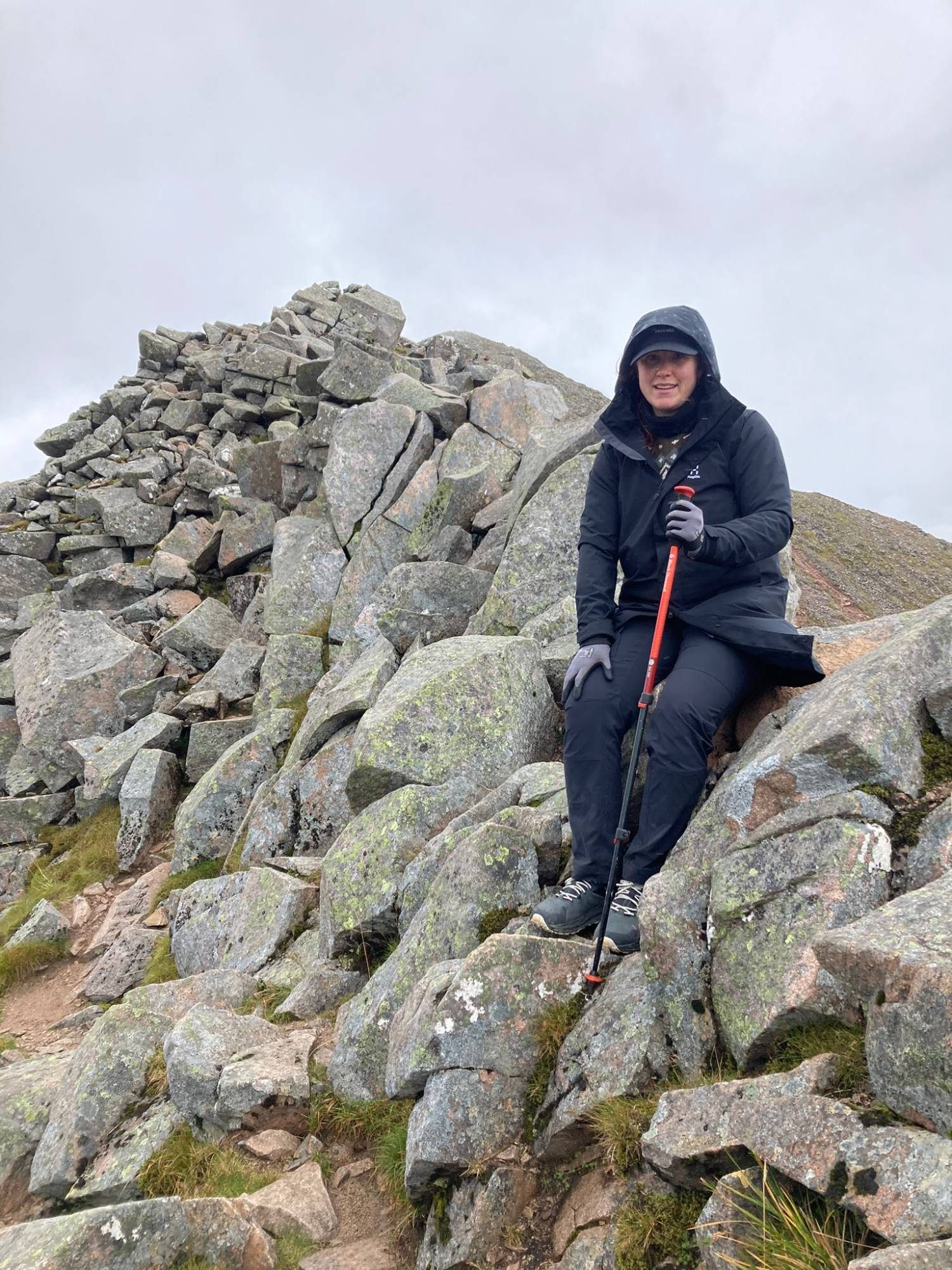 Kristine sitting on a granite boulder on the ridge with a trekking pole