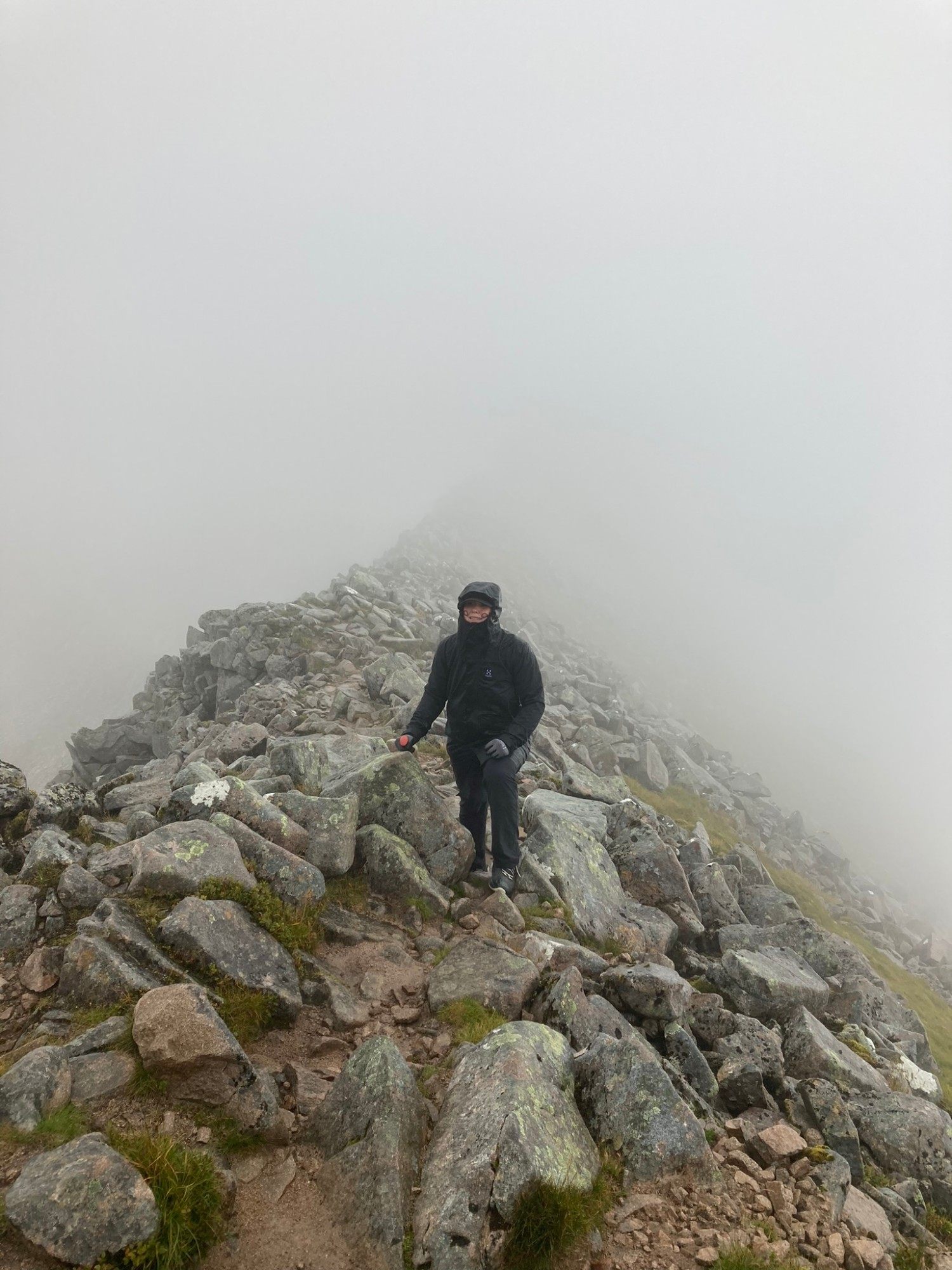 Kristine wrapped up in a hood and buff climbing a boulder field in thick cloud