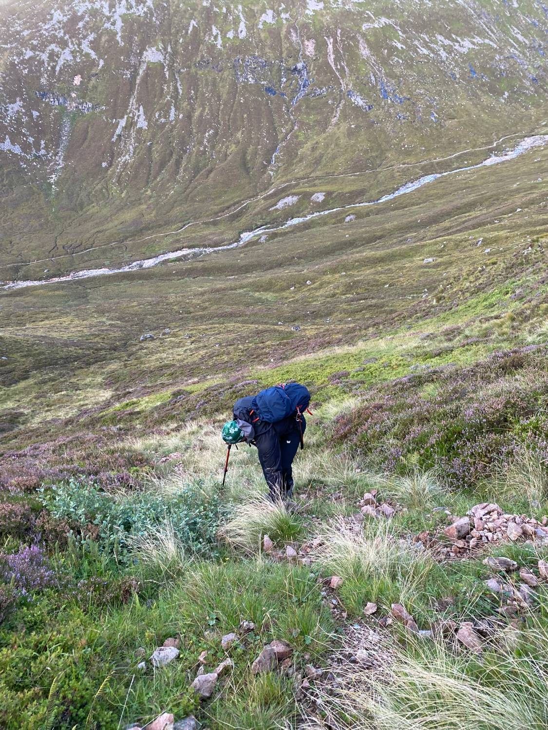 Leif bent over his trekking pole on a steep heather slope off the path, with the path in the glen far below