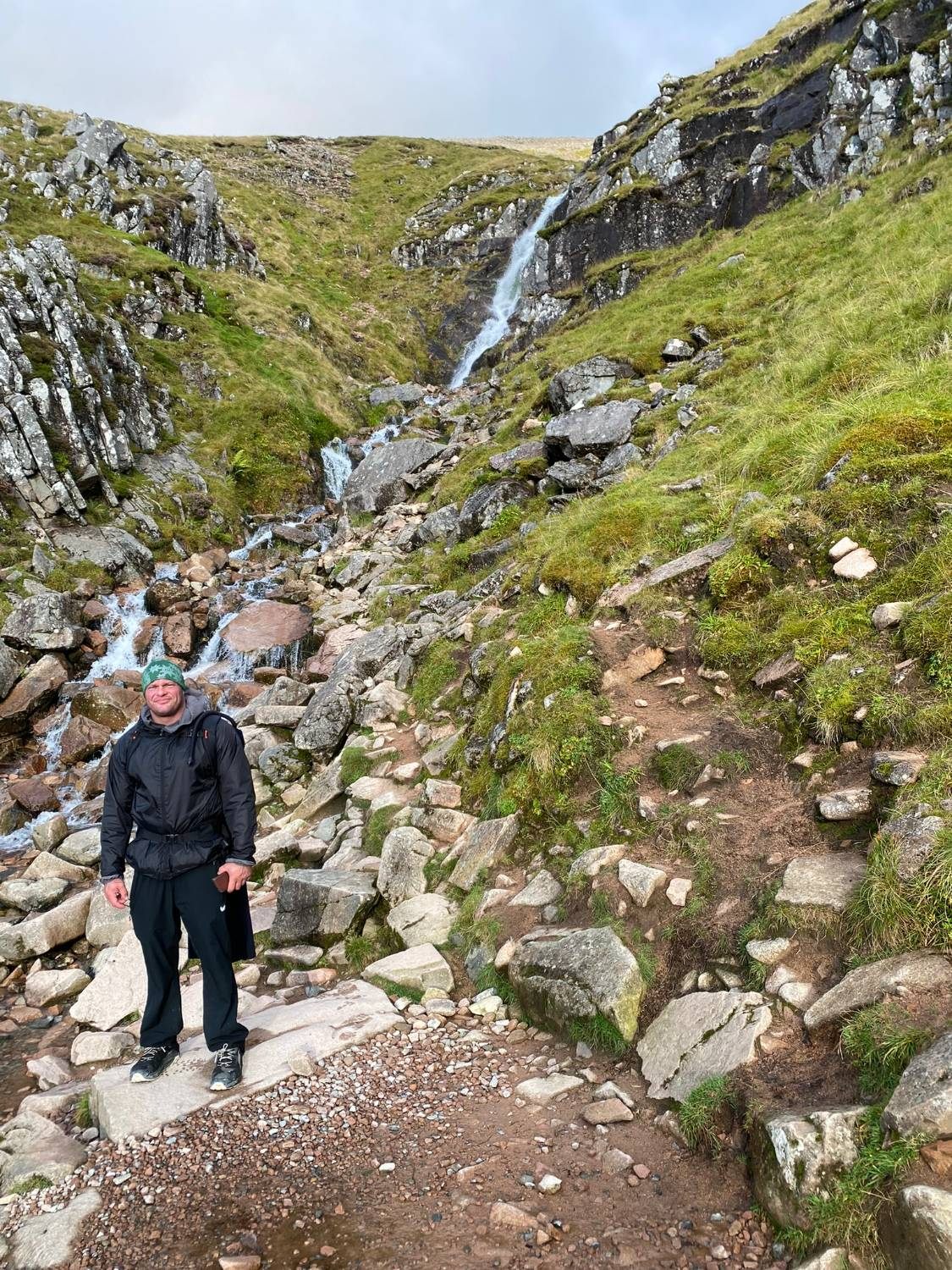 Leif in a green beanie standing on rocks in front of a waterfall