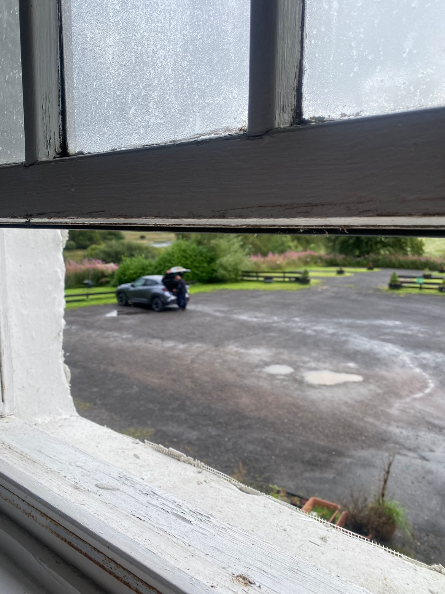 View through an old sash window of The Luib Hotel onto the car park, with our grey rental car and pink flowers