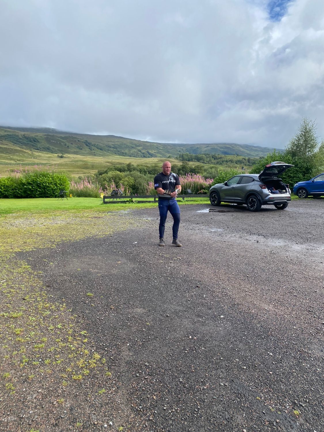 Leif in a T-shirt chalking his hands on the hotel car park, with hills and the rental car behind