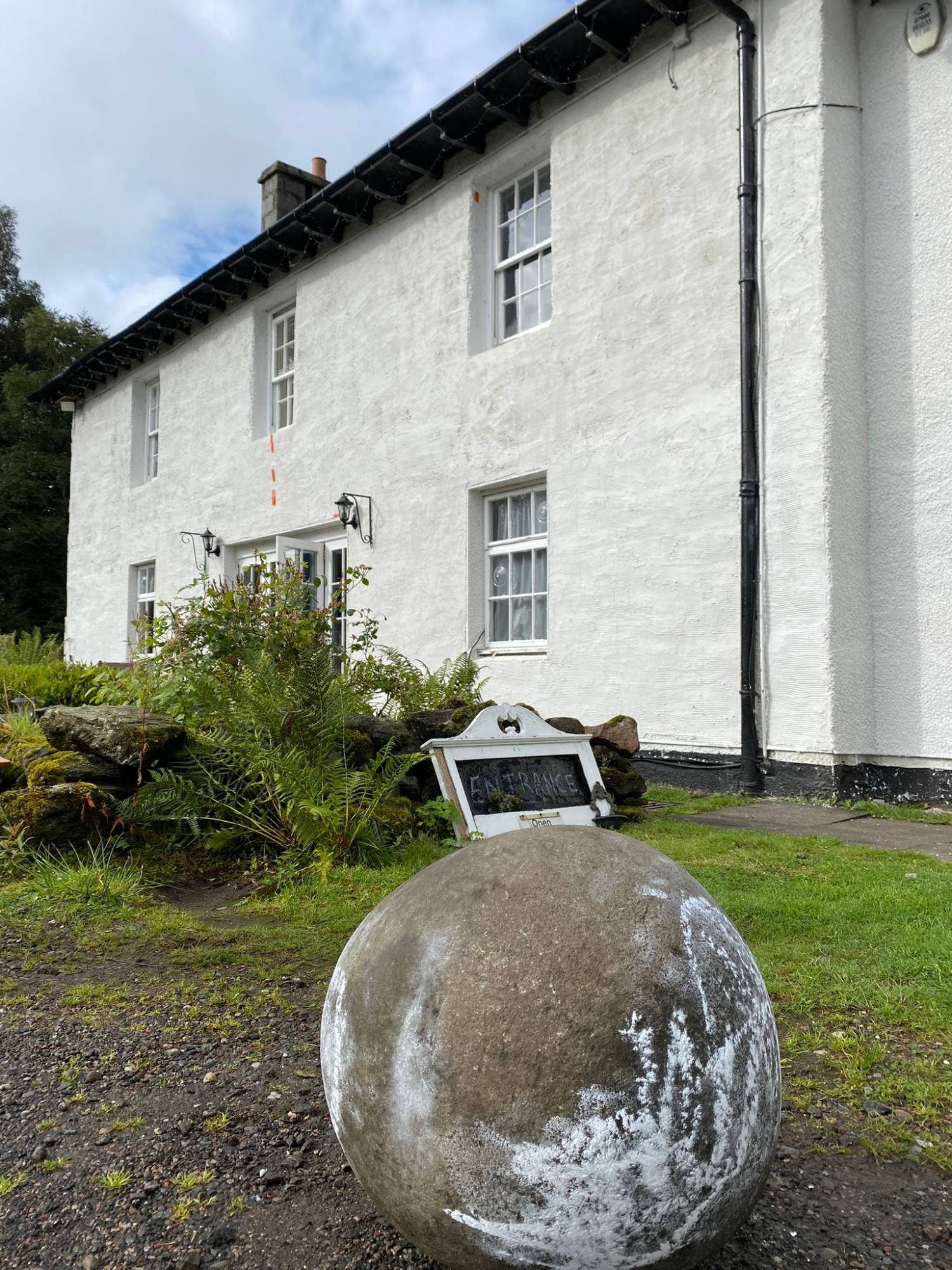 The round MacGregor Stone, dusted with chalk, on the gravel in front of the white Luib Hotel