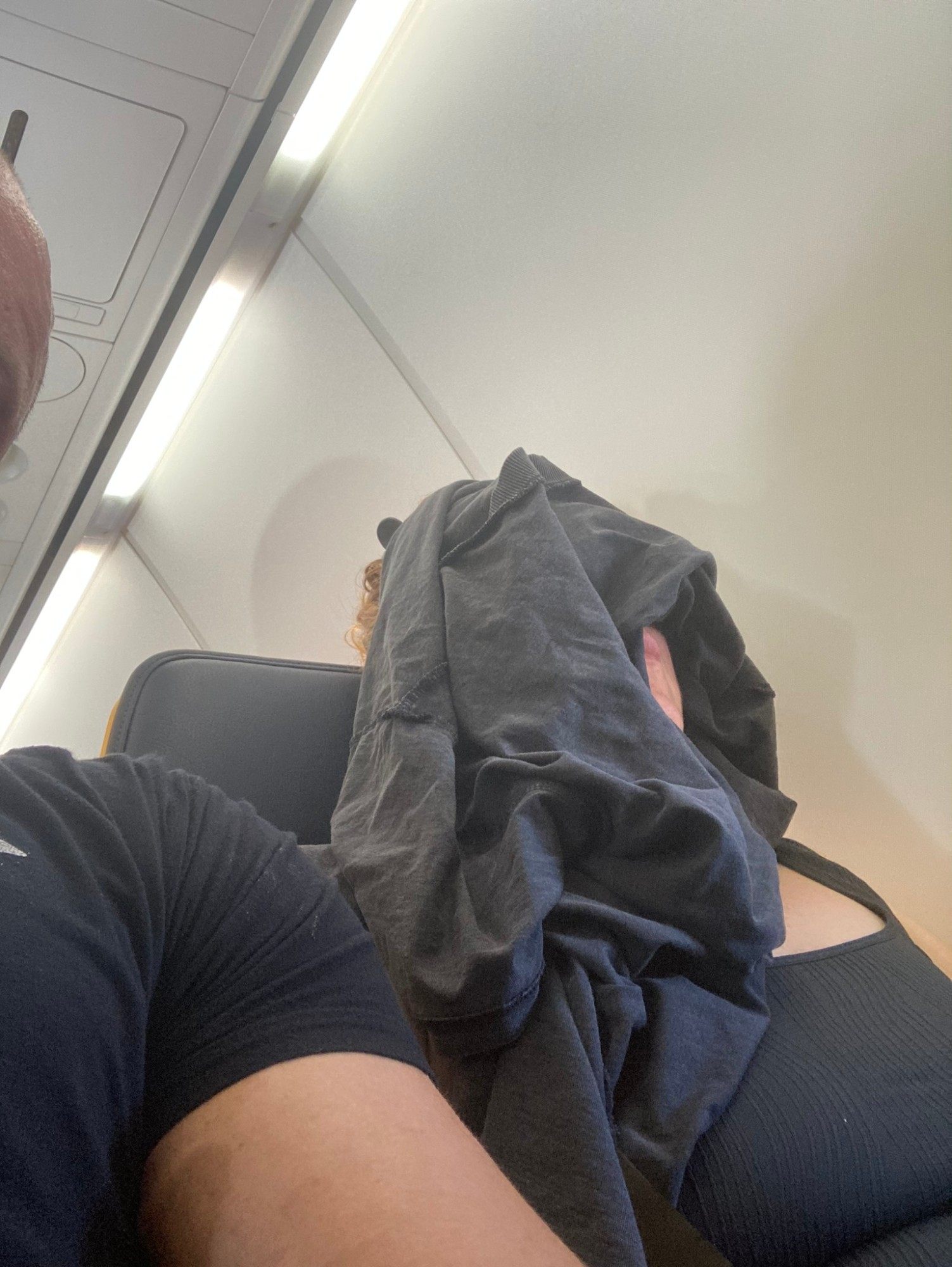 Kristine asleep in a plane seat with a T-shirt pulled over her face