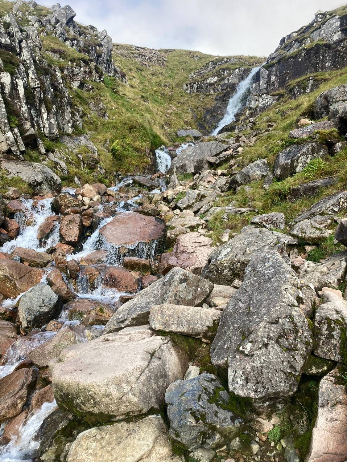 A waterfall tumbling down a rocky gully into a boulder-filled stream