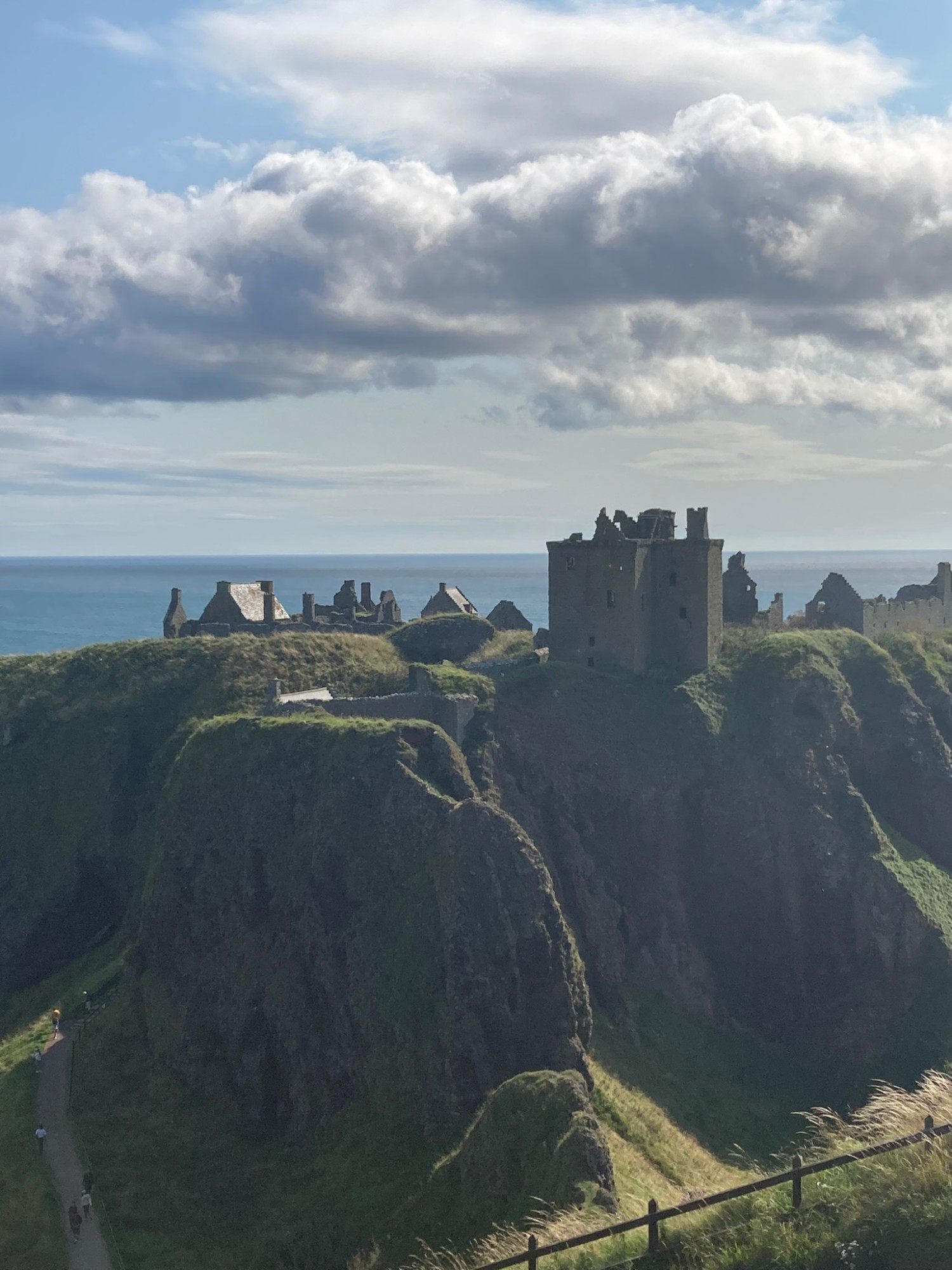 The ruins of Dunnottar Castle on a steep green headland above the North Sea, with the path leading down on the left