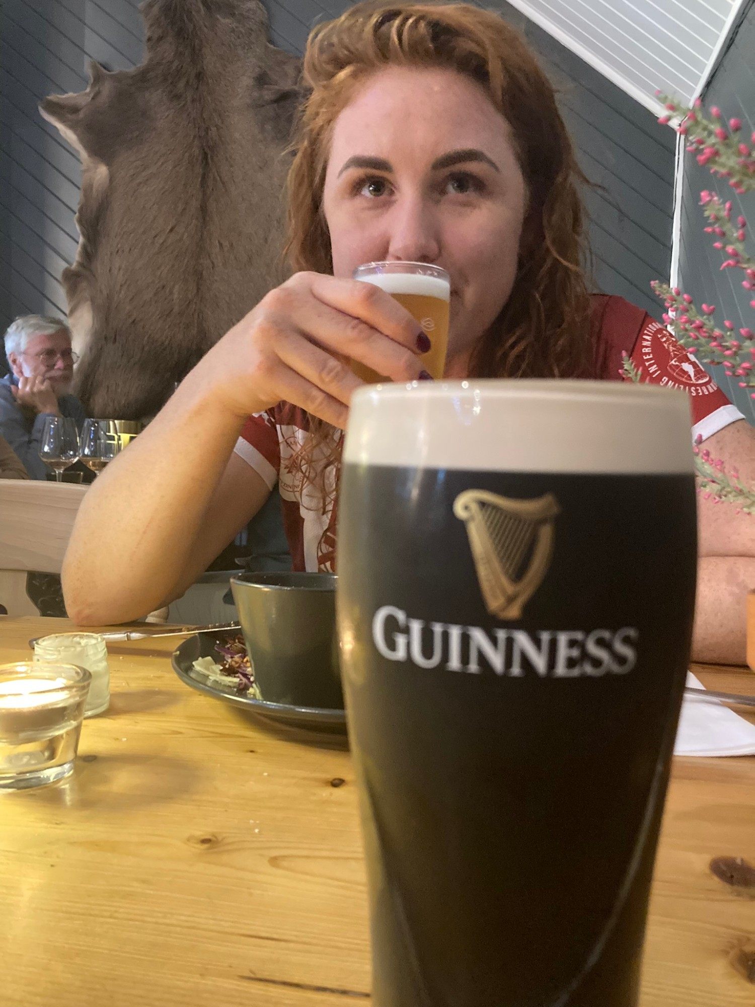 Kristine sipping a beer at a wooden table, with a pint of Guinness in the foreground
