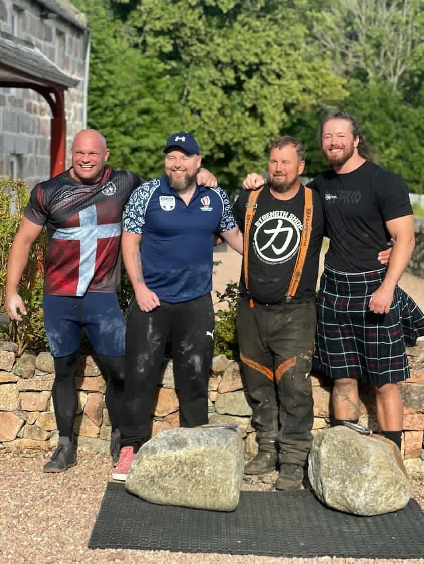Four lifters with their arms around each other behind the Dinnie Stones