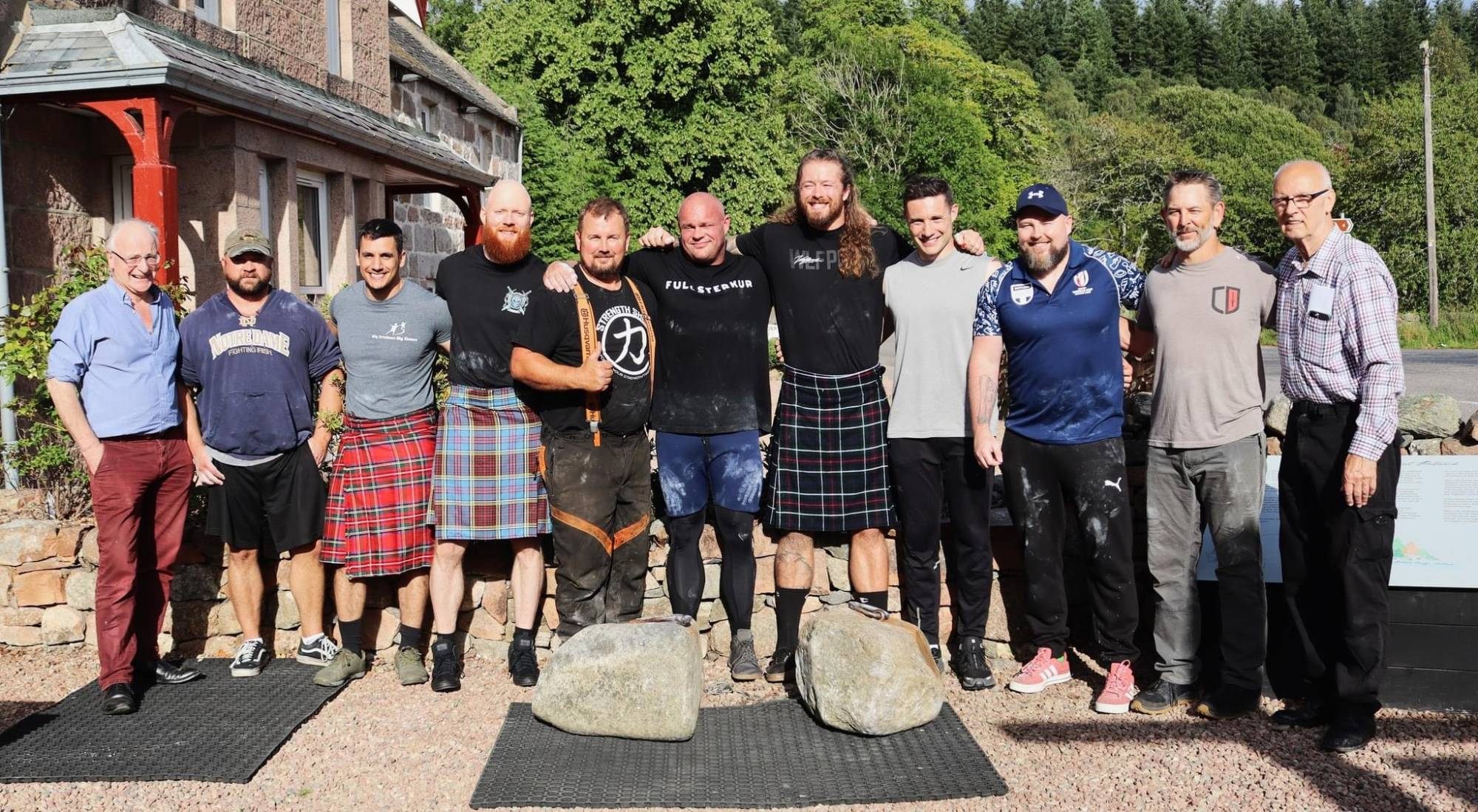 Group photo of lifters and onlookers standing behind the two Dinnie Stones at Potarch