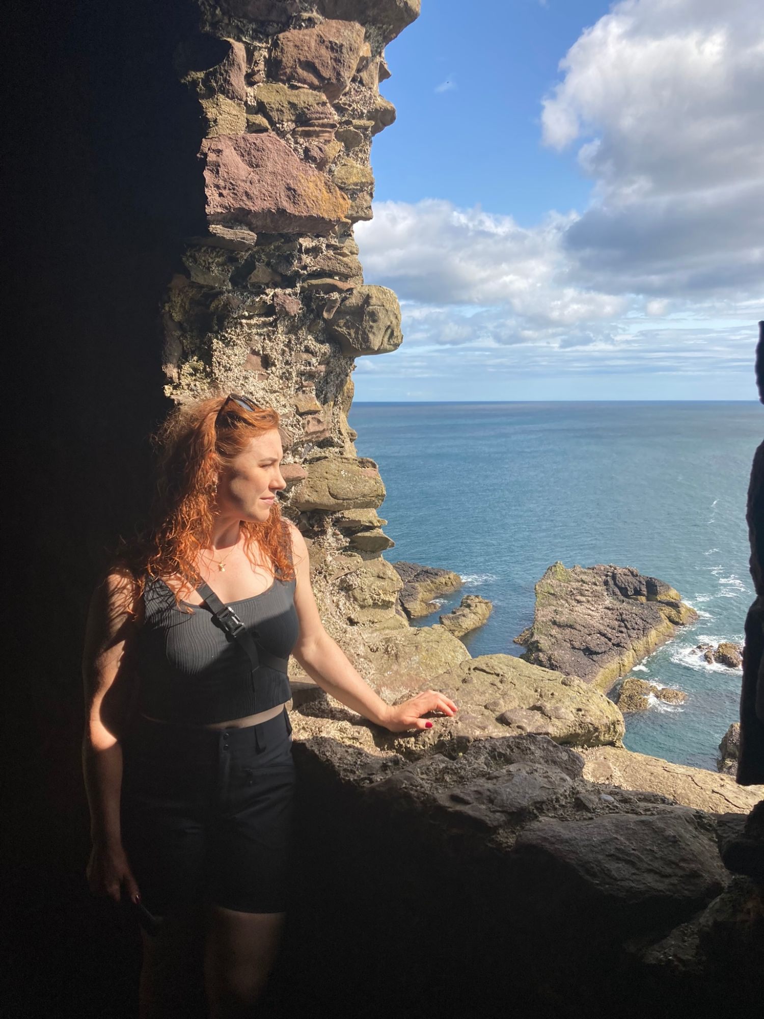 Kristine standing in a large ruined window opening, looking out at the sea and the rocks below